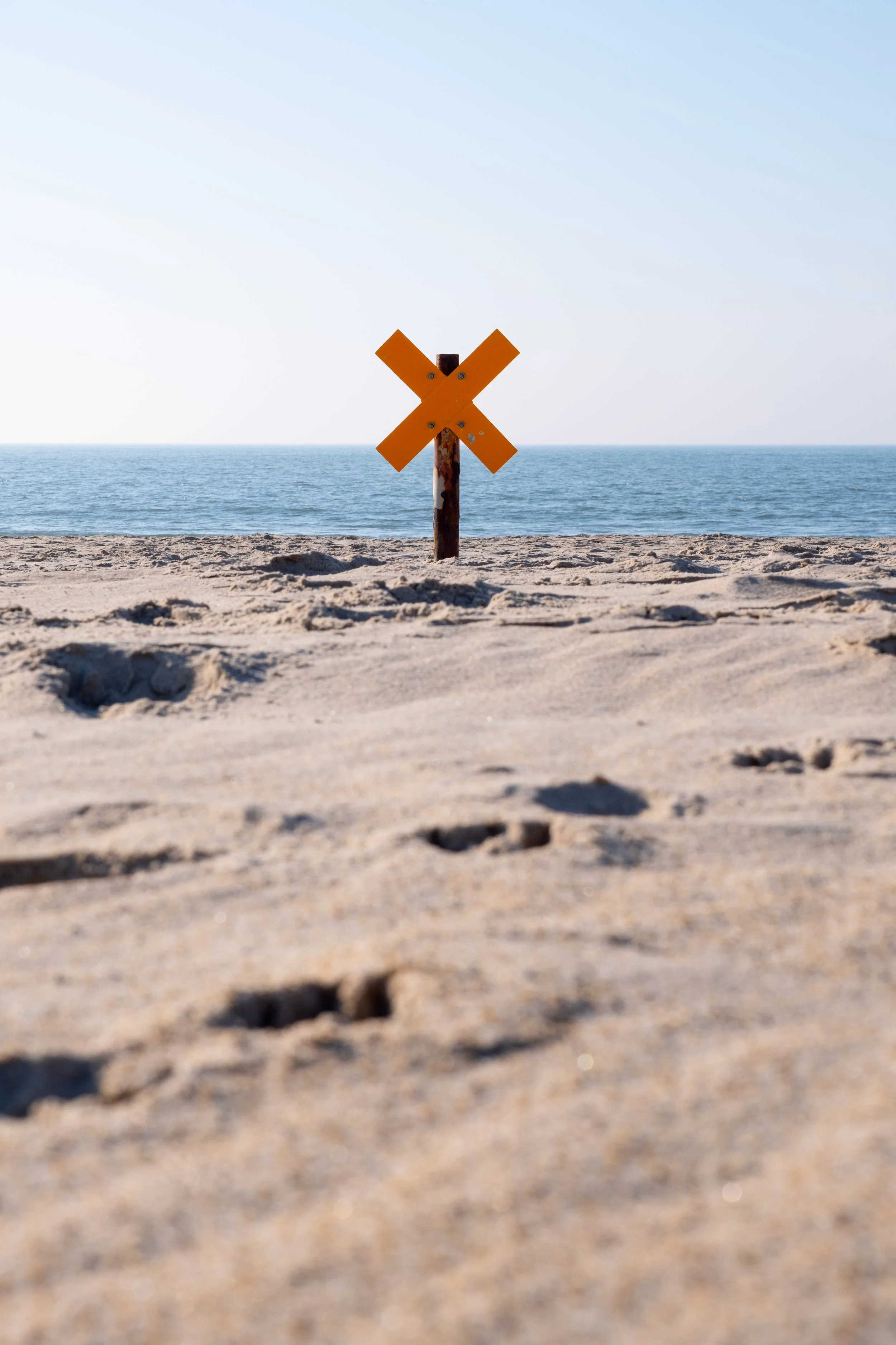 Ein gelbes X-Schild am Strand mit Meer im Hintergrund.
