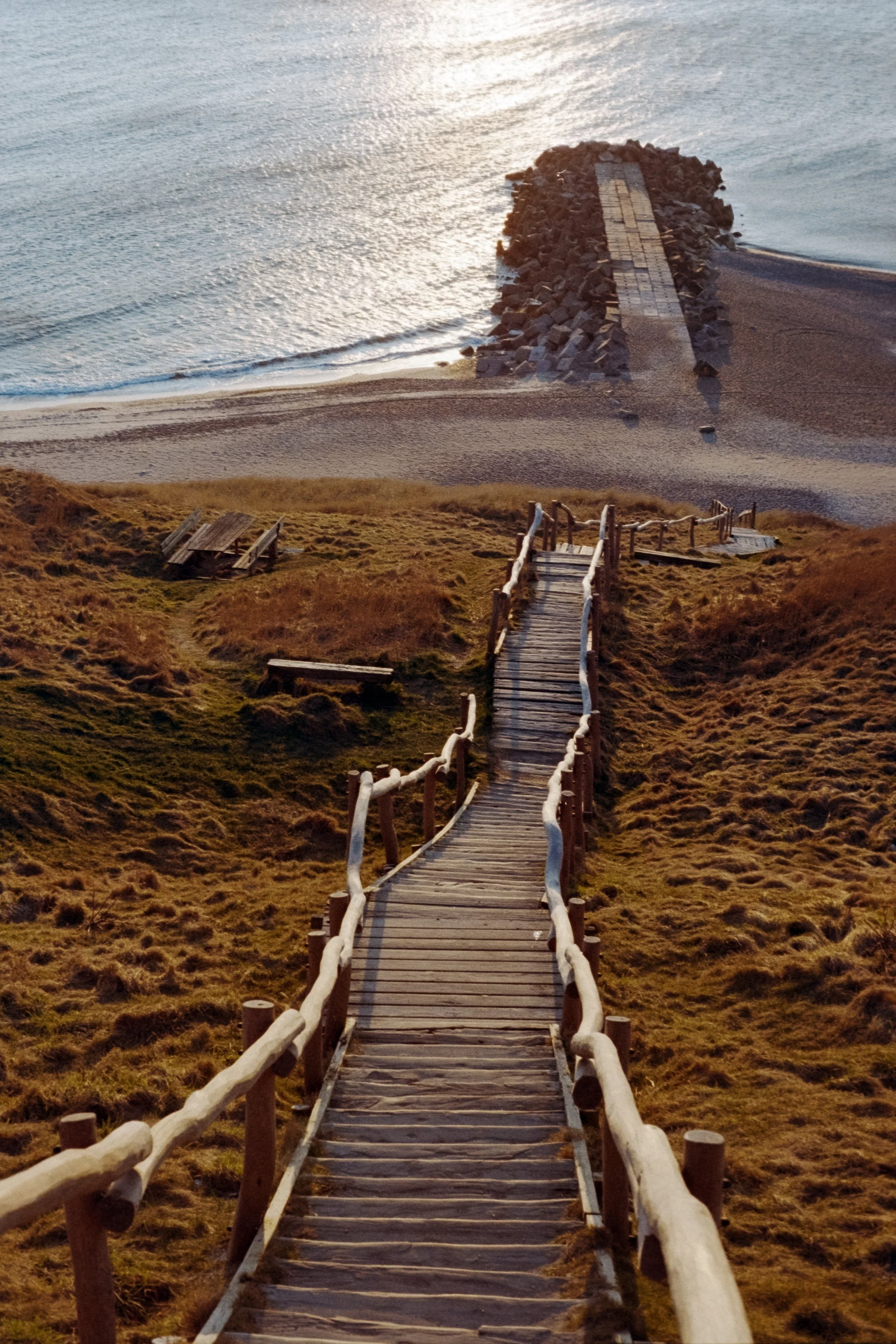 Das Bild zeigt eine alte Holztreppe, die entlang einer Steilküste in Dänemark zum Strand führt. Die Farben in diesem Bild sind sehr warm.