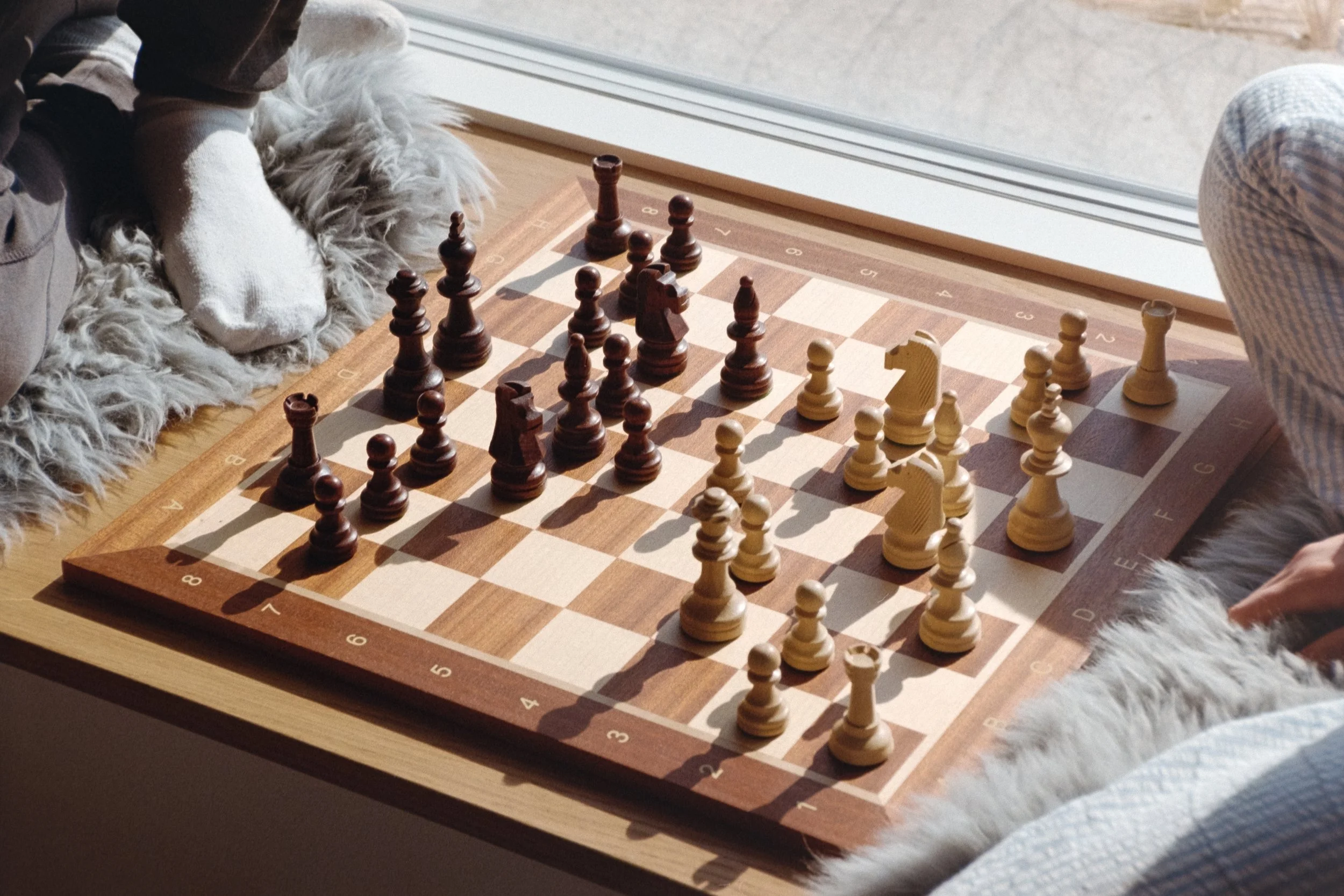Diese analoge Fotografie zeigt zwei Freunde, die im Urlaub in Søndervig miteinander auf einem Holzschachbrett mit Holzfiguren Schach spielen.