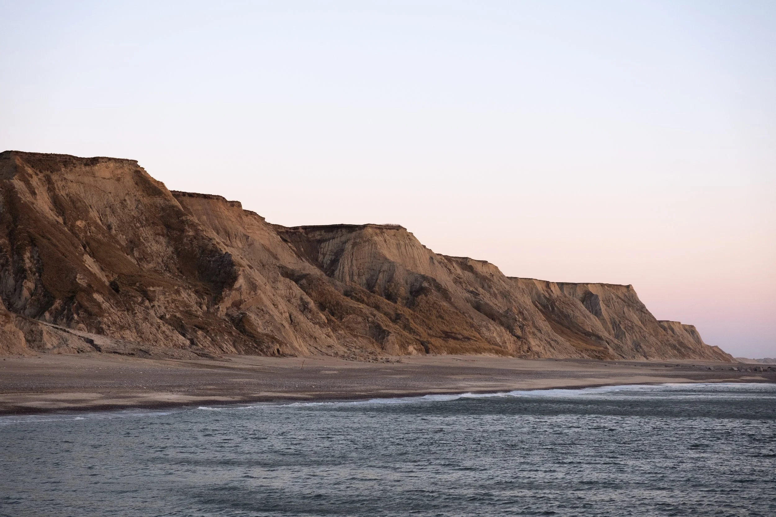 Felsige Küste bei Sonnenuntergang mit ruhigem Meer im Vordergrund.