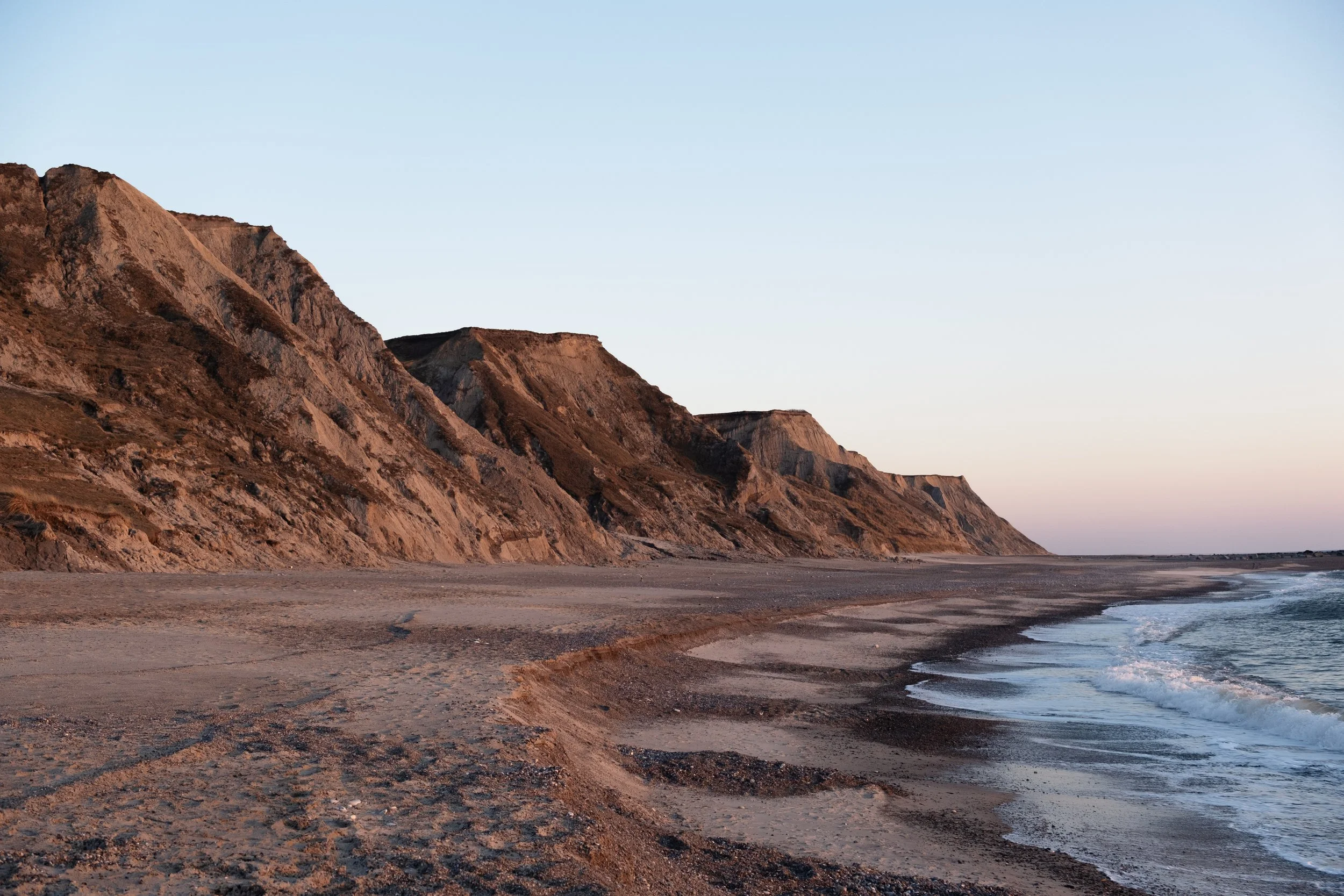 Steilküste am Strand bei Sonnenuntergang, mit ruhigem Meer und klarem Himmel.