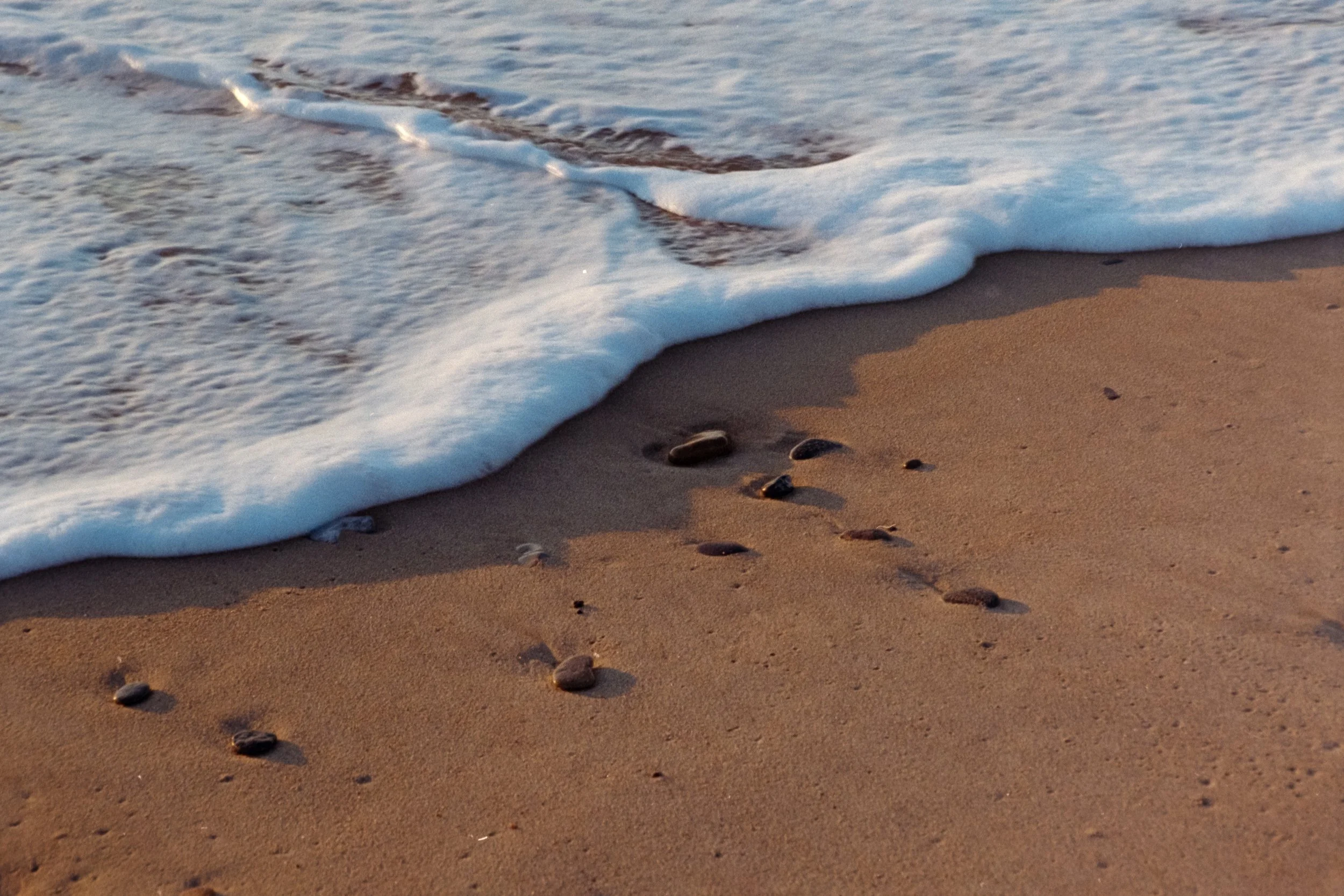 Diese analoge Fotografie zeigt eine Welle, die auf dem Strand in Søndervig ein paar Muscheln und Steine wegspült.