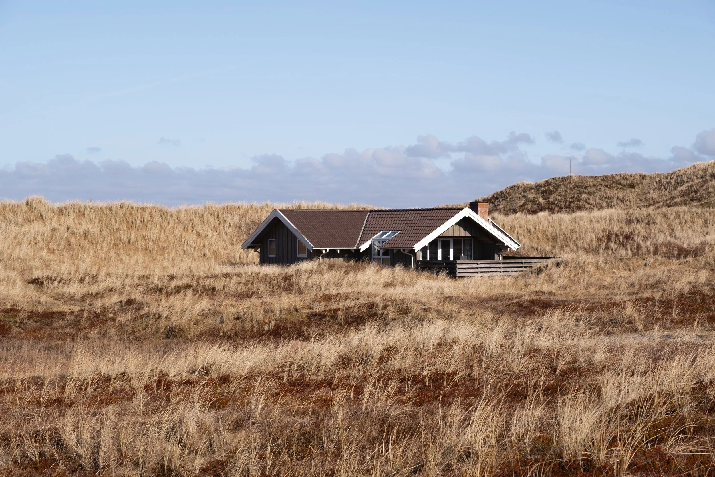 Das Zentrum dieser Fotografie ist von einem flachen Haus belegt. Dieses liegt mitten in der Dünen Landschaft von Søndervig, Dänemark.