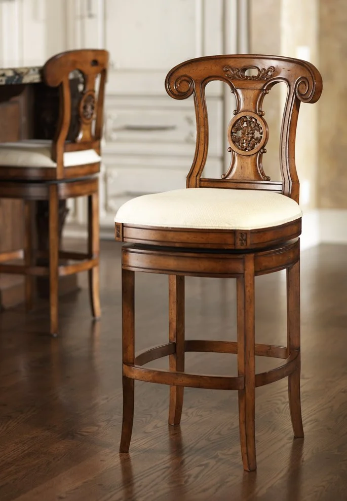 A wooden chair with an ornate backrest and a cushioned seat in a dining room, next to a table with other wooden chairs in the background.
