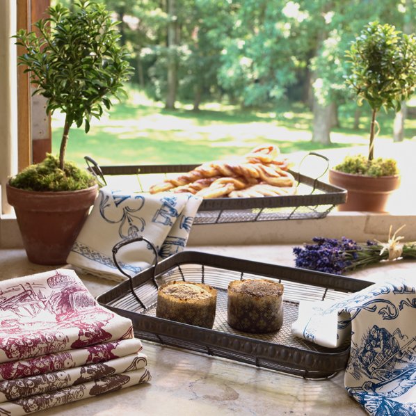Sunlit kitchen window sill with potted plants, bread on a drying rack, and baking supplies on the countertop.