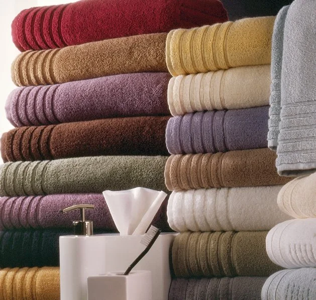 Stacked folded towels in various colors on a shelf with a soap dispenser and a tissue box in front.