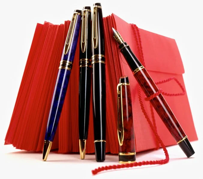 Four pens with gold accents, red notebooks, and red paper clips on a white background.