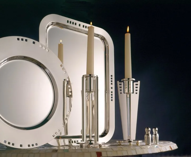 A collection of white and silver dining and decorative trays, candle holders with lit candles, and salt and pepper shakers on a mosaic-tiled surface against a dark background.