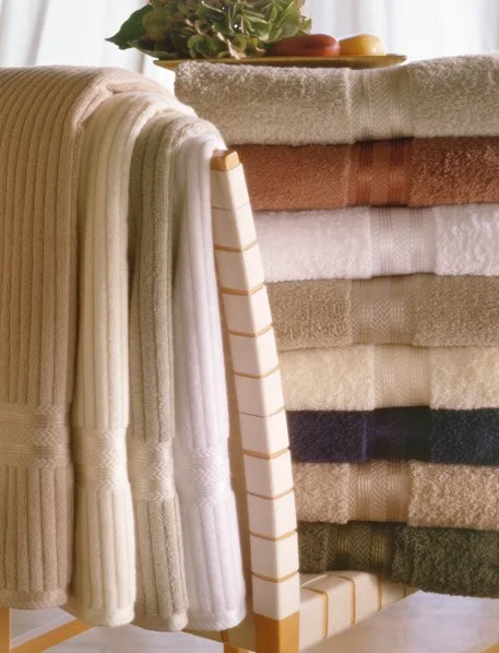 Stack of folded towels in various colors and patterns, with a tray of decorative fruit and greenery on a side table.