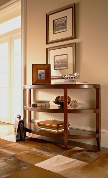 A wooden console table with three shelves, decorated with framed photos, a decorative object, and books, against a wall with two framed pictures.