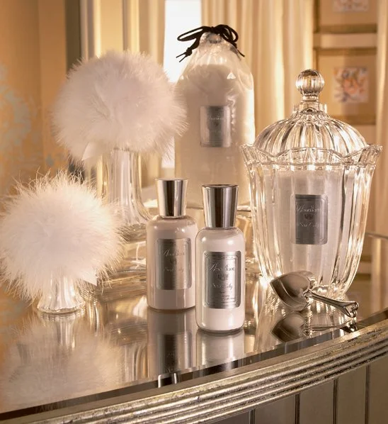 Display of elegant glass containers and vessels, some with white fluffy decorations, on a shiny silver surface.