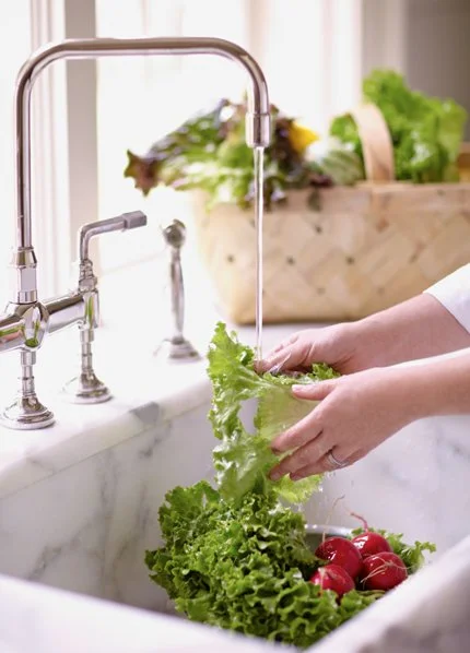 Person washing fresh lettuce and radishes in a kitchen sink with a modern faucet.