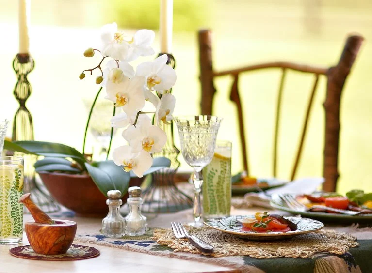 Elegant dining table setup with white orchids, glassware, plates with food, and a rustic background