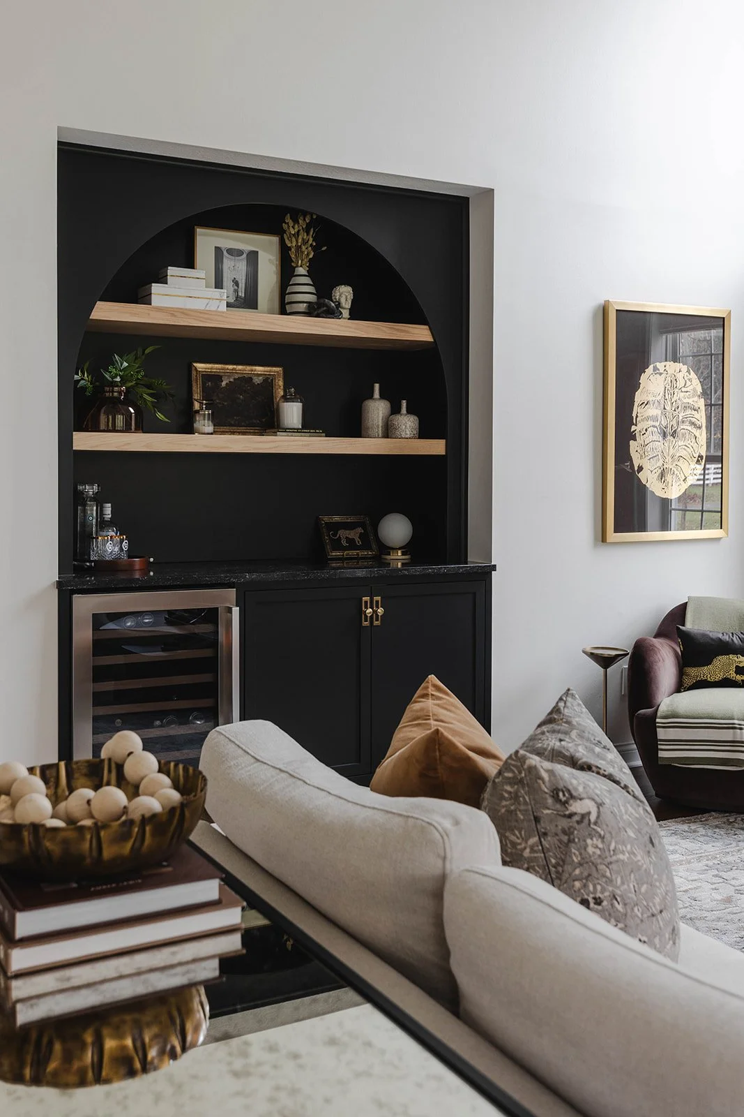 Living room with built-in black cabinet with wooden shelves, artwork on the walls, and a variety of decorative pillows on a cream sofa.