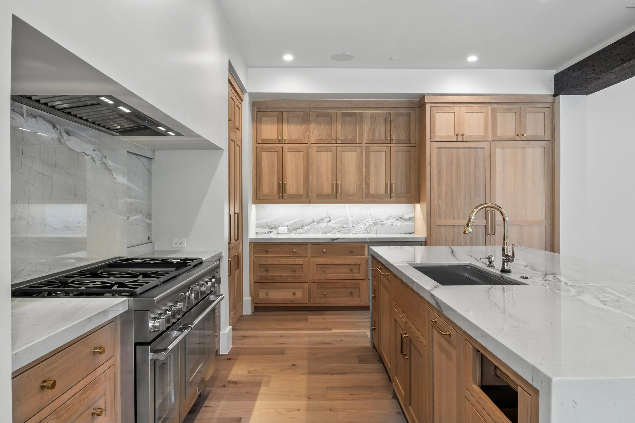 Modern kitchen with wooden cabinets, marble countertops, stainless steel oven, and hardwood flooring.