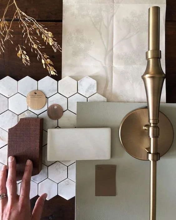 Interior design mood board with hexagonal tiles, fabric swatches, paint sample, decorative objects, and a brass lamp.