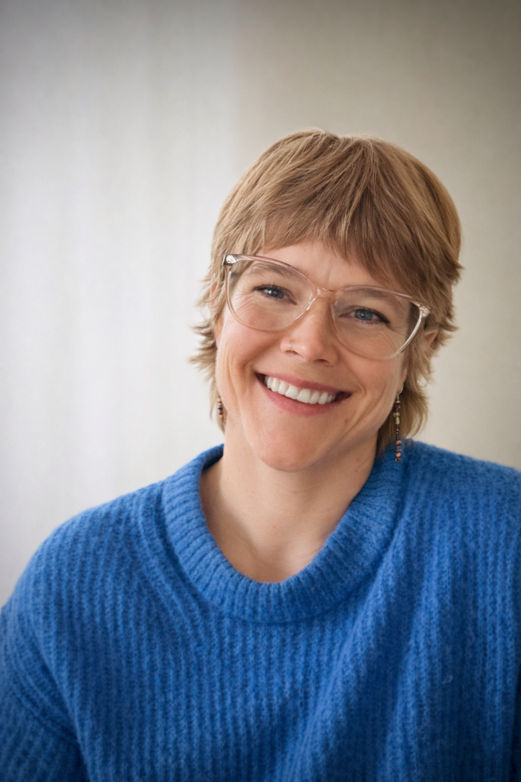Smiling woman with short blonde hair, wearing glasses and a blue sweater.