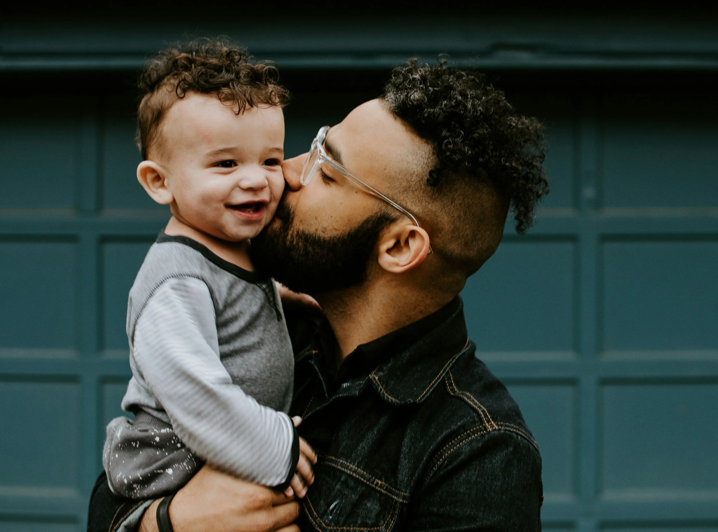 A man with curly hair and glasses holding a smiling toddler with curly hair and a painted face