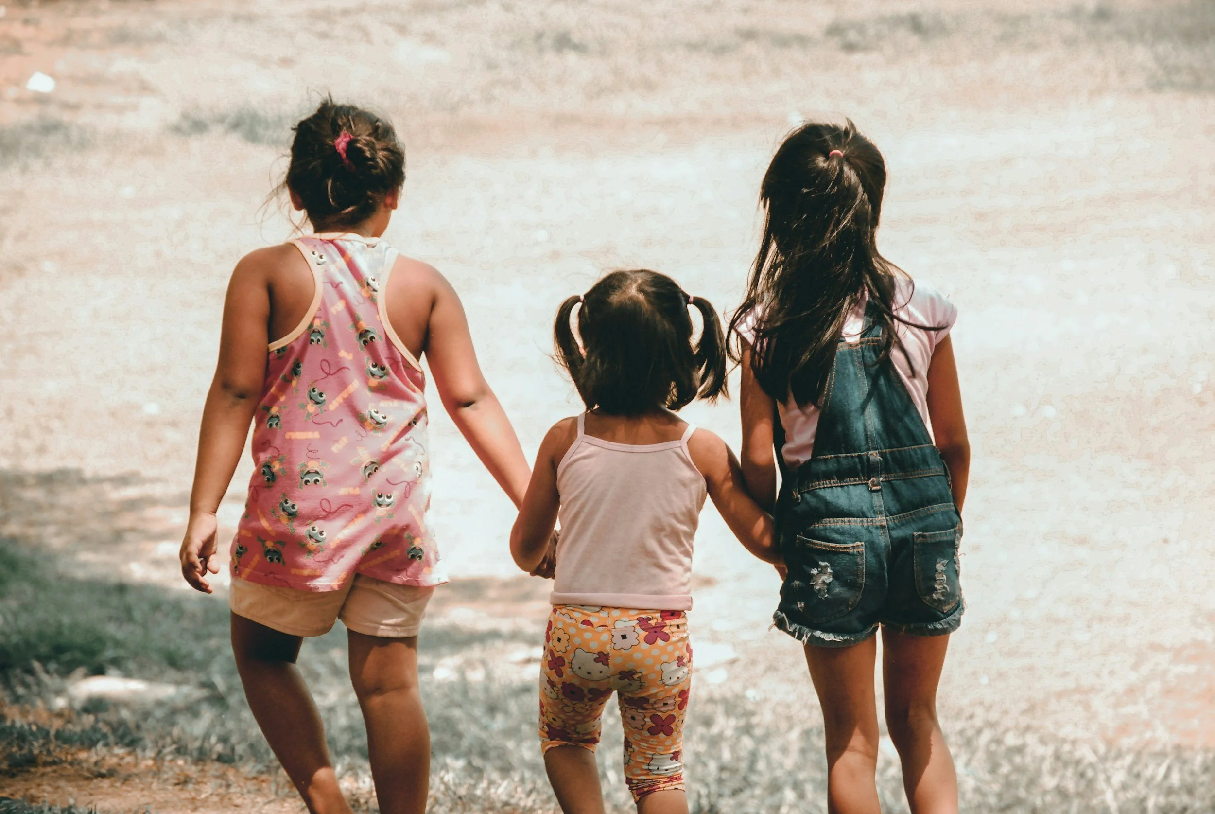 Four children walking together on a sandy beach, seen from behind.