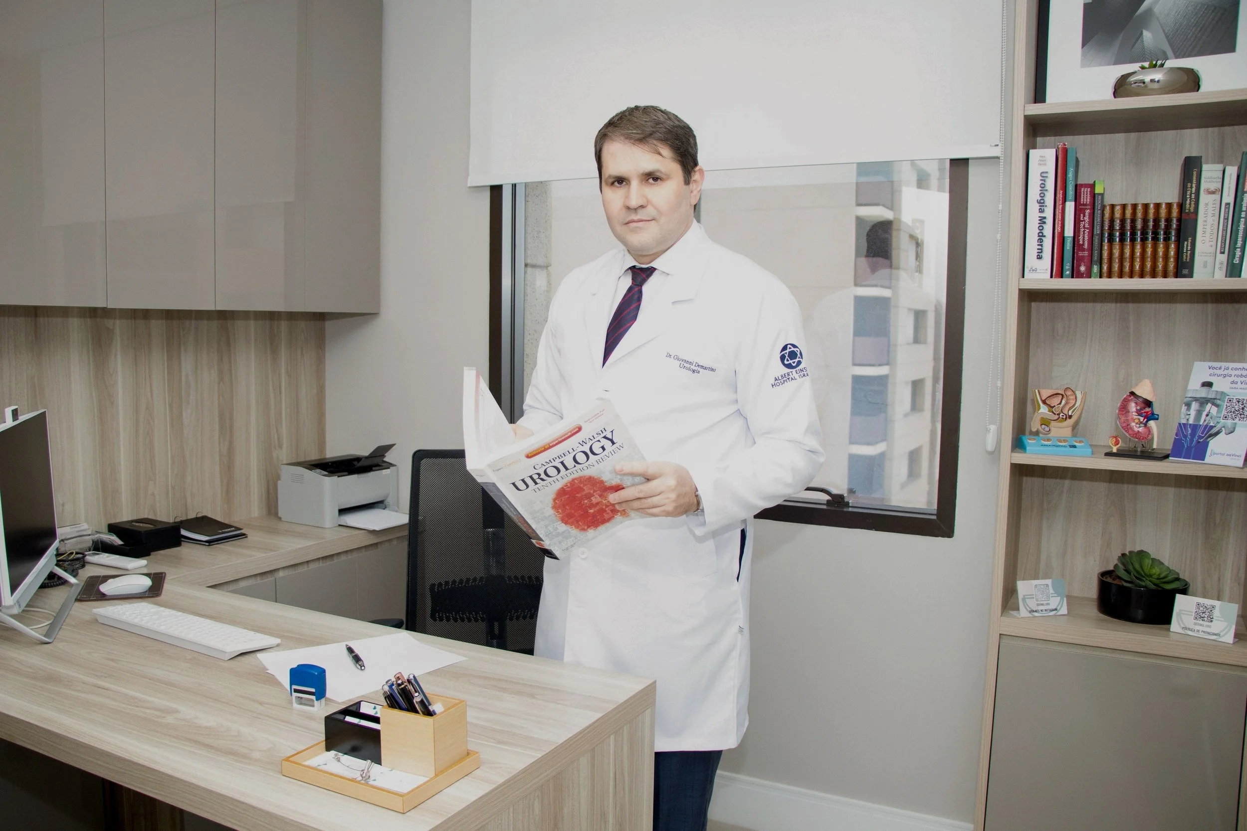 Homem médico de bata branca segurando livro sobre urologia em escritório.