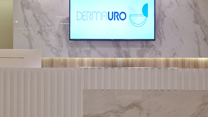 Tela de TV exibindo o logo do Clínica DermaUro em uma parede de mármore.