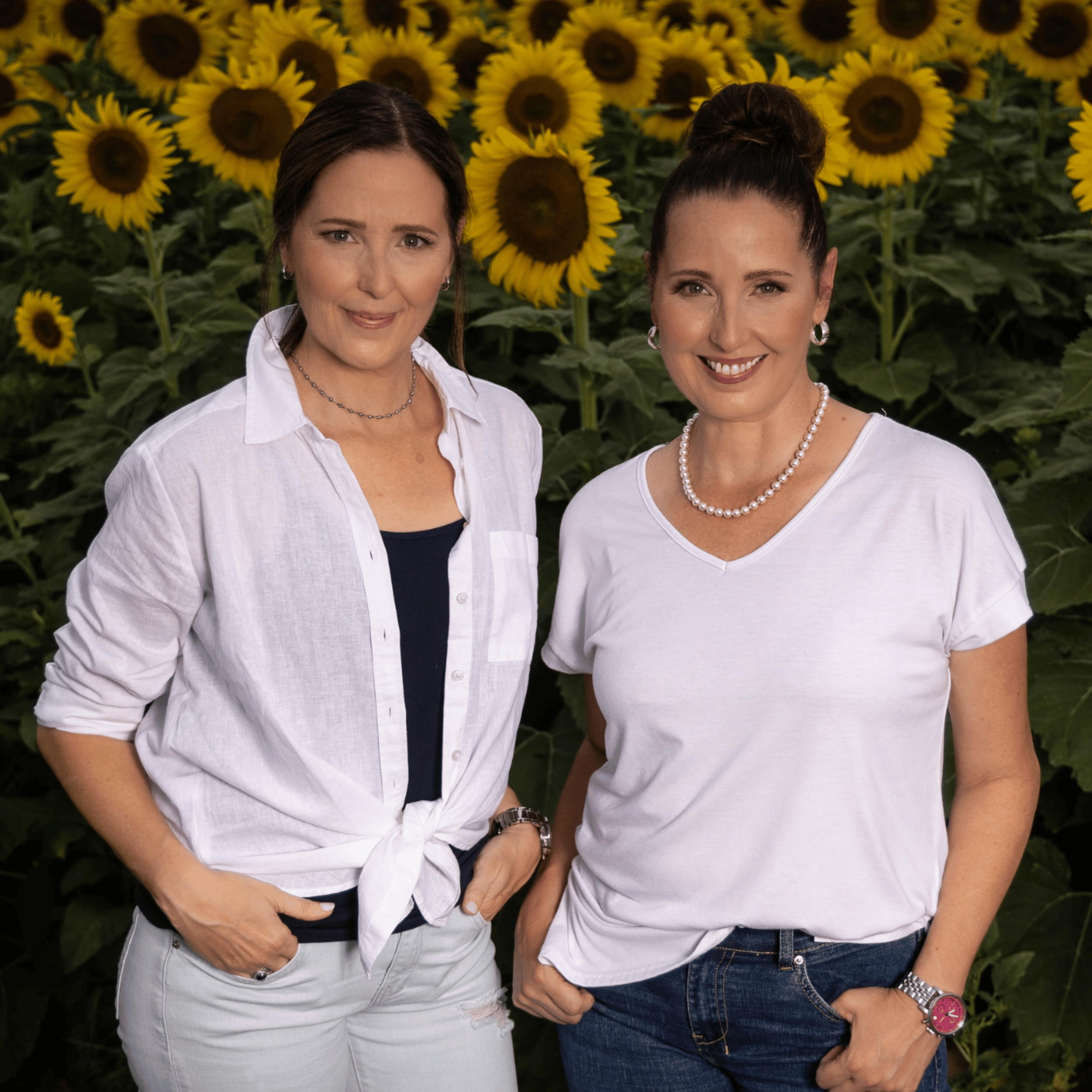 Two women standing side by side both wearing white tops and jeans.