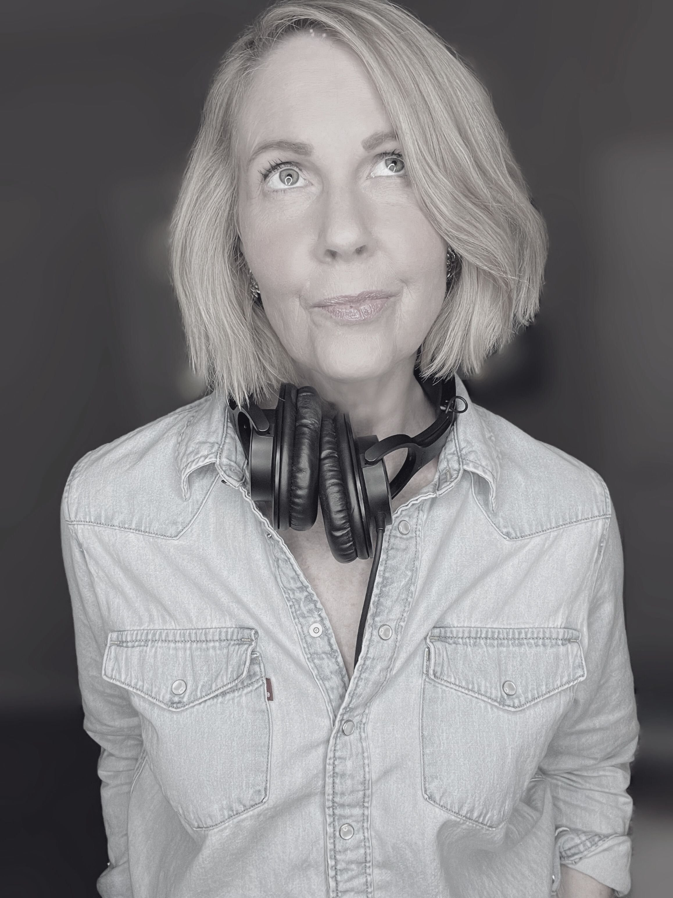 A photo of Lori Massicot looking up wearing headphones around her neck representing a thought bubble above her head. She is wearing a levis jean shirt. The image is black and white.