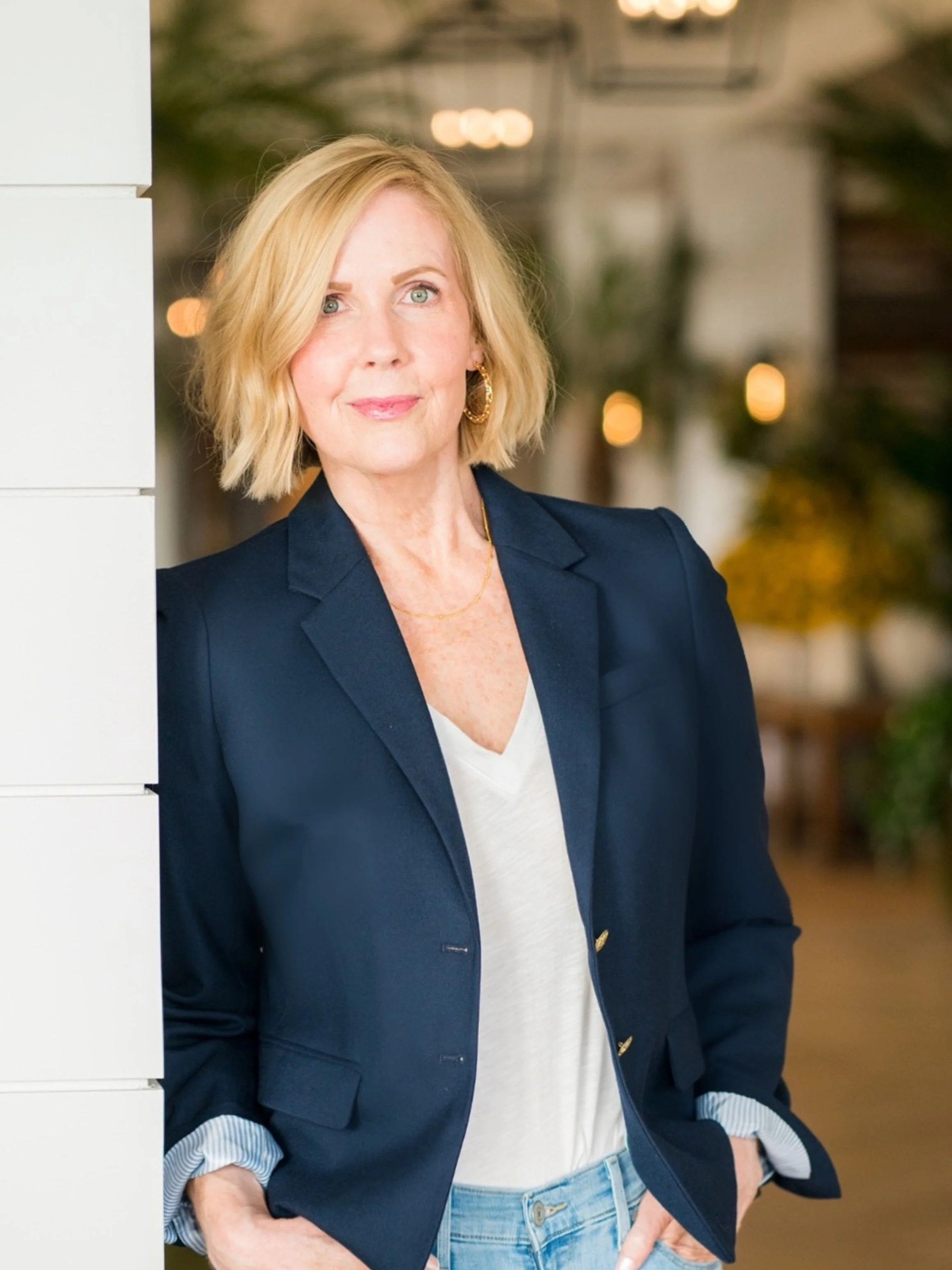 Portrait of Lori Massicot, host of the To 50 and Beyond podcast, wearing a navy blazer and white top, standing indoors and looking calmly toward the camera.
