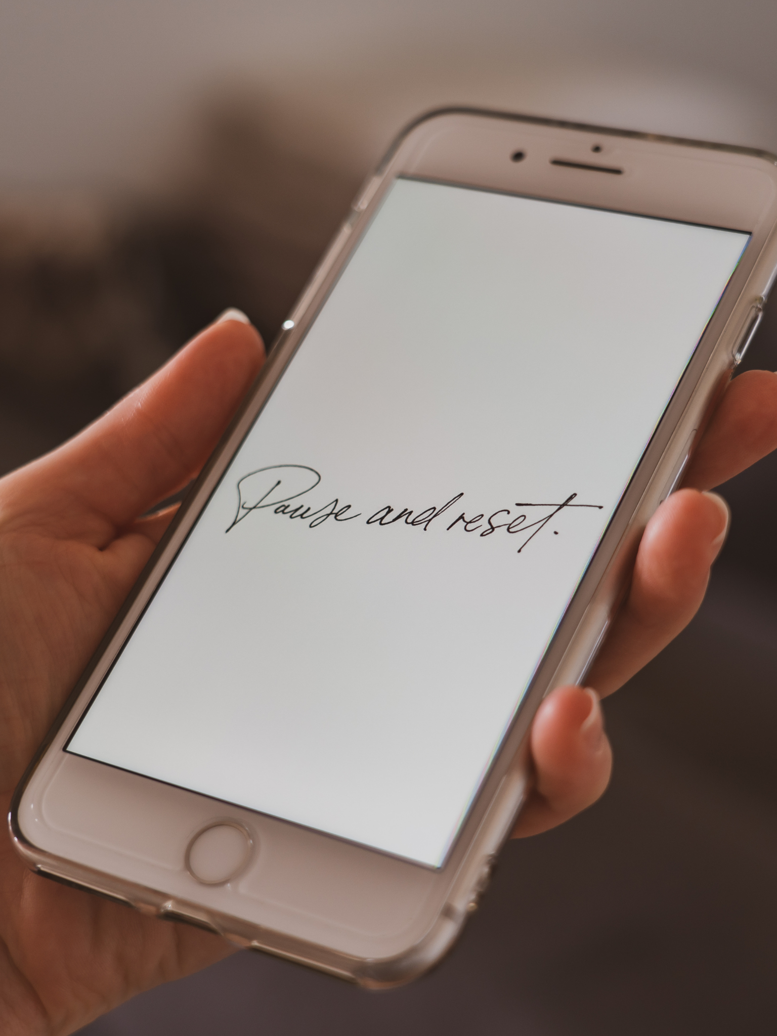 Image shows a woman's hand holding a white iPhone with the text "pause and reset" on the screen.