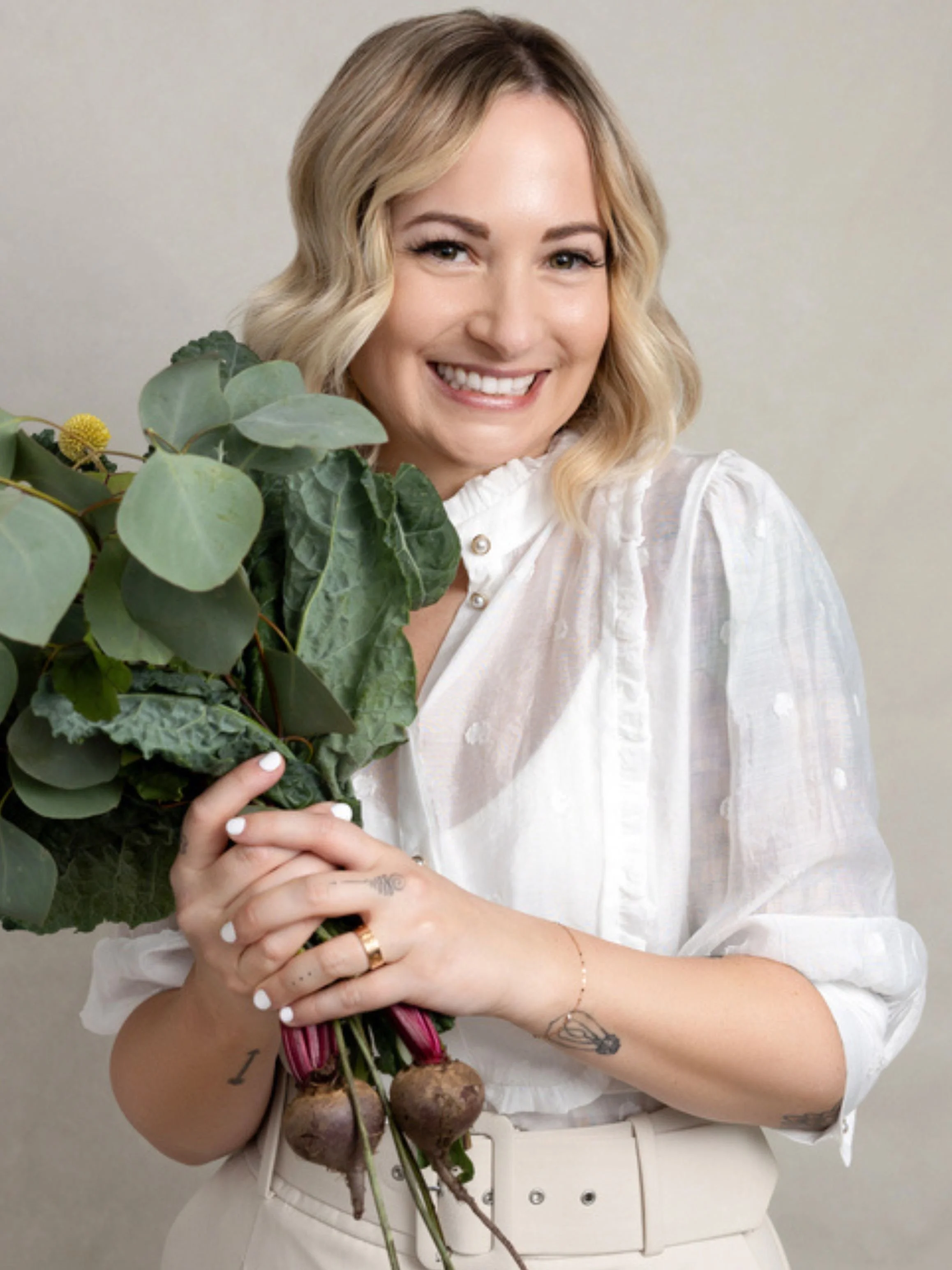Dr. Brooke Scheller smiles while holding fresh flowers, featured on the To 50 and Beyond podcast discussing managing sobriety through nutrition, supplements, gut health, and alcohol-free living for midlife women.