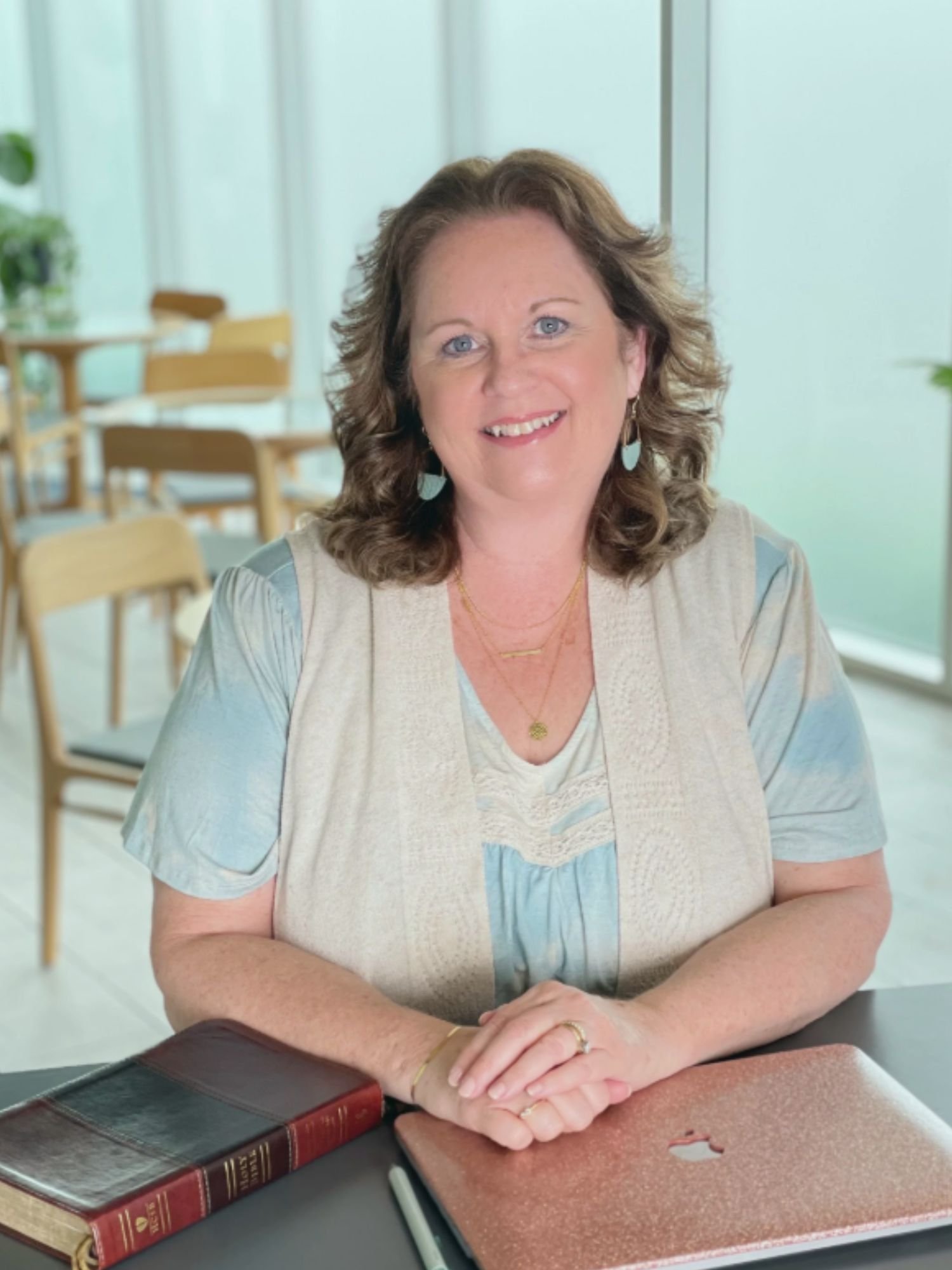 Karen Ehman smiling at a table with a Bible and laptop, author and speaker discussing people pleasing, boundaries, and faith for women in midlife.