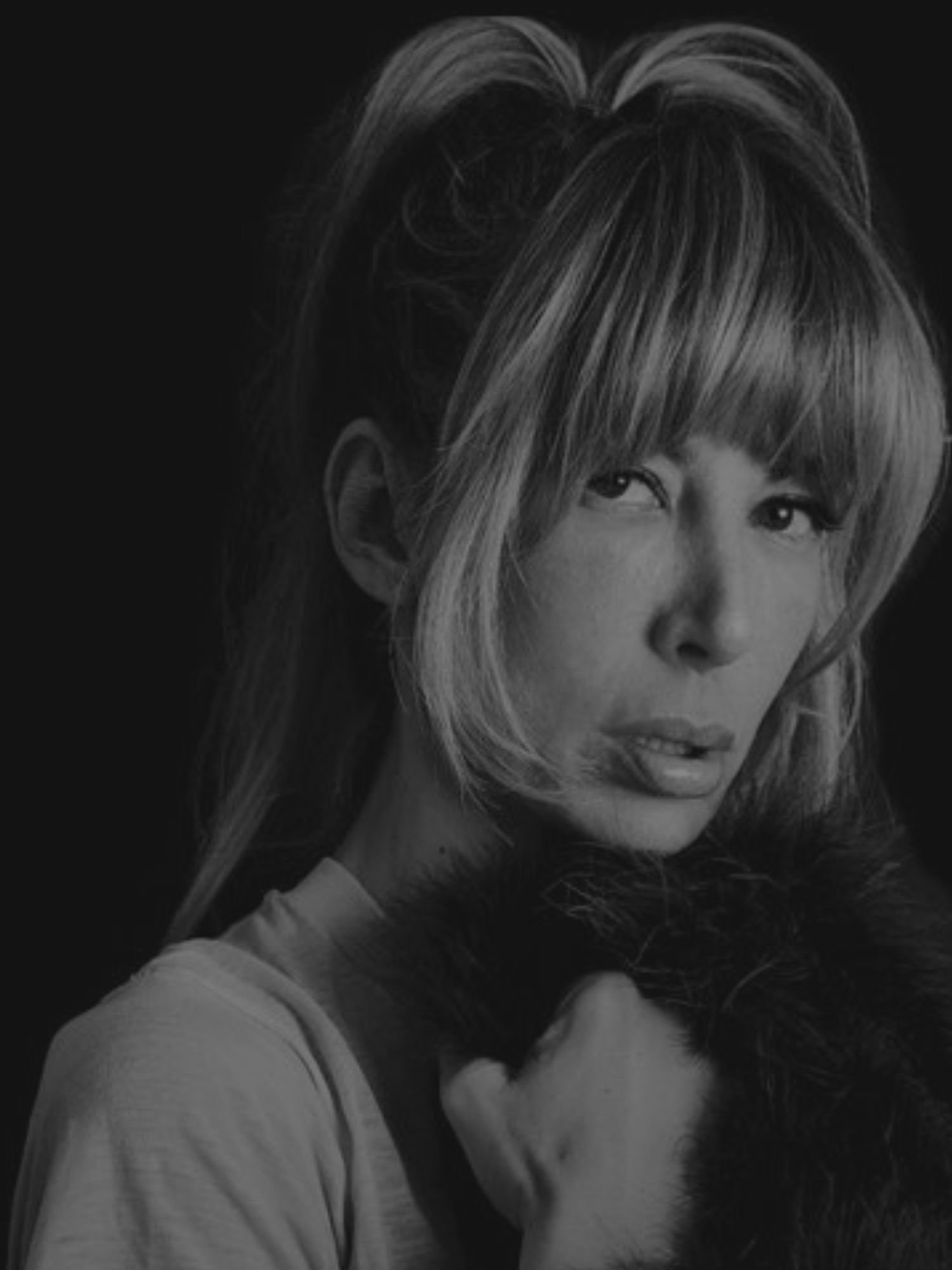 A photo of Amy Dresner looking at the camera. The photo is black and white and Amy's hair is blonde with bangs and she is holding a fur blanket.
