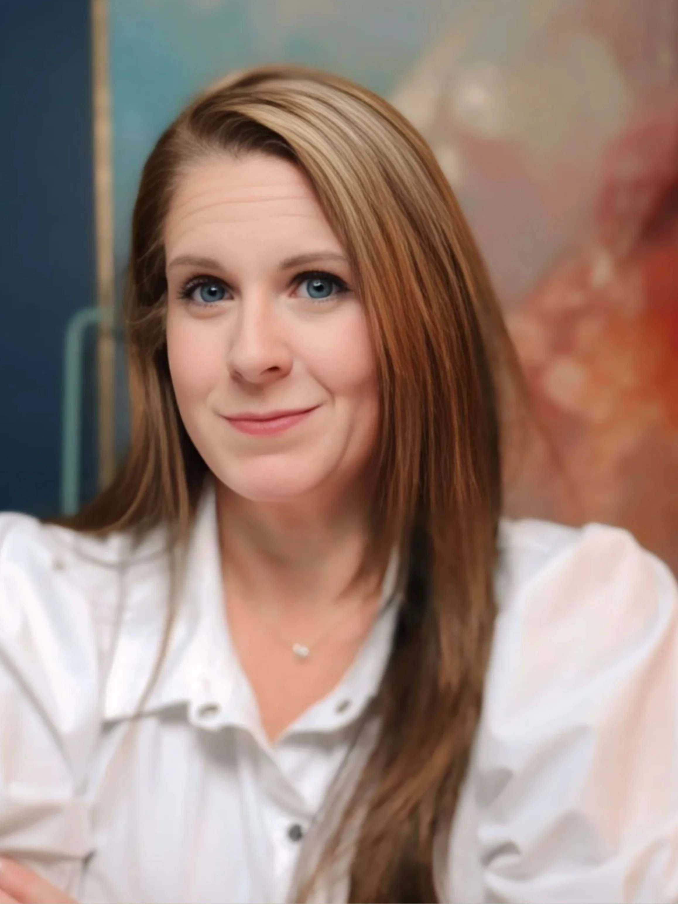 Portrait of a woman with long light brown hair wearing a white blouse, photographed indoors.