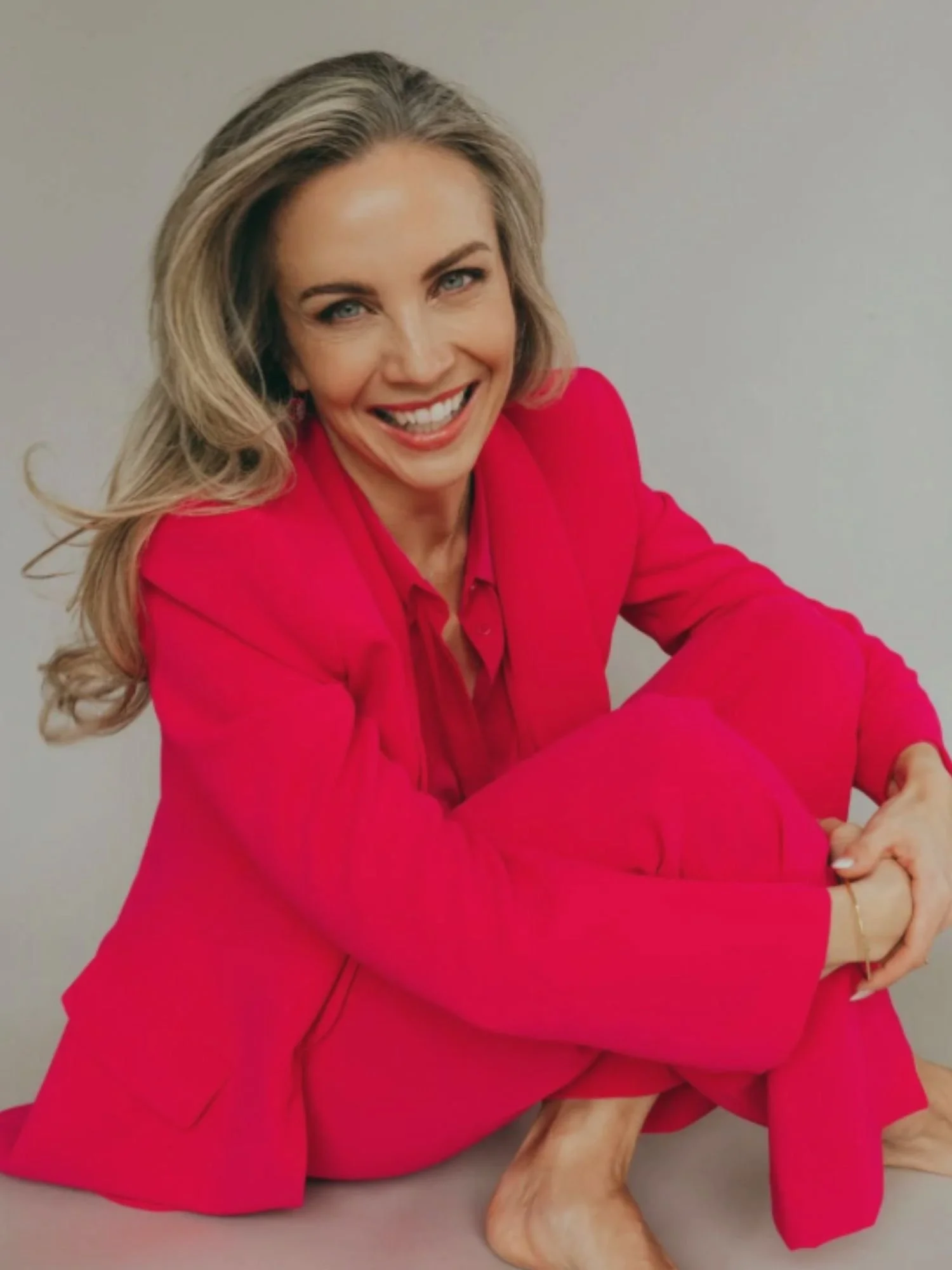 Lindsay Sutherland Bohl smiling while seated on the floor, wearing a bright pink suit, representing leadership in alcohol free living for women.