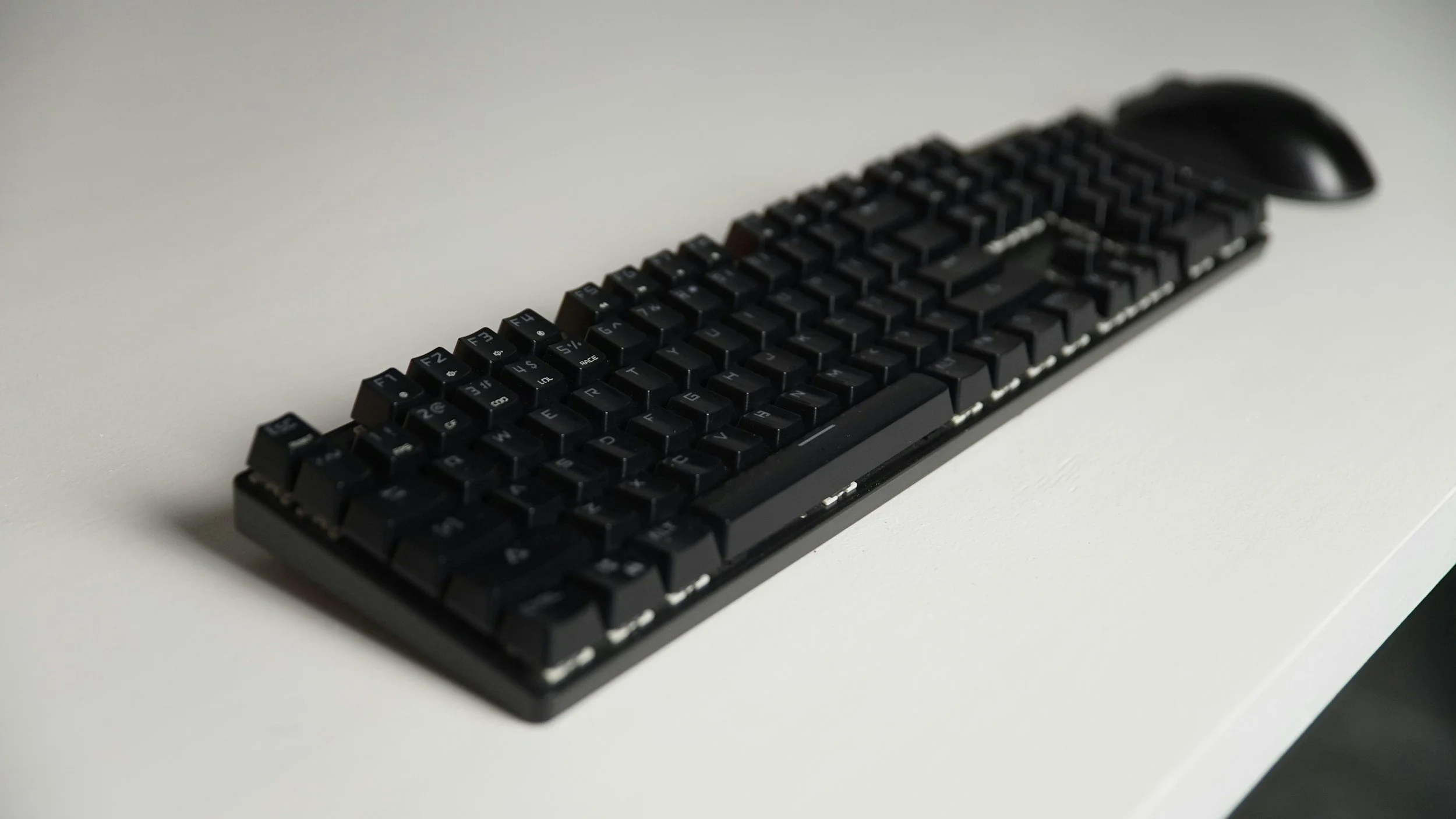 Black computer keyboard with a mouse on a white desk.
