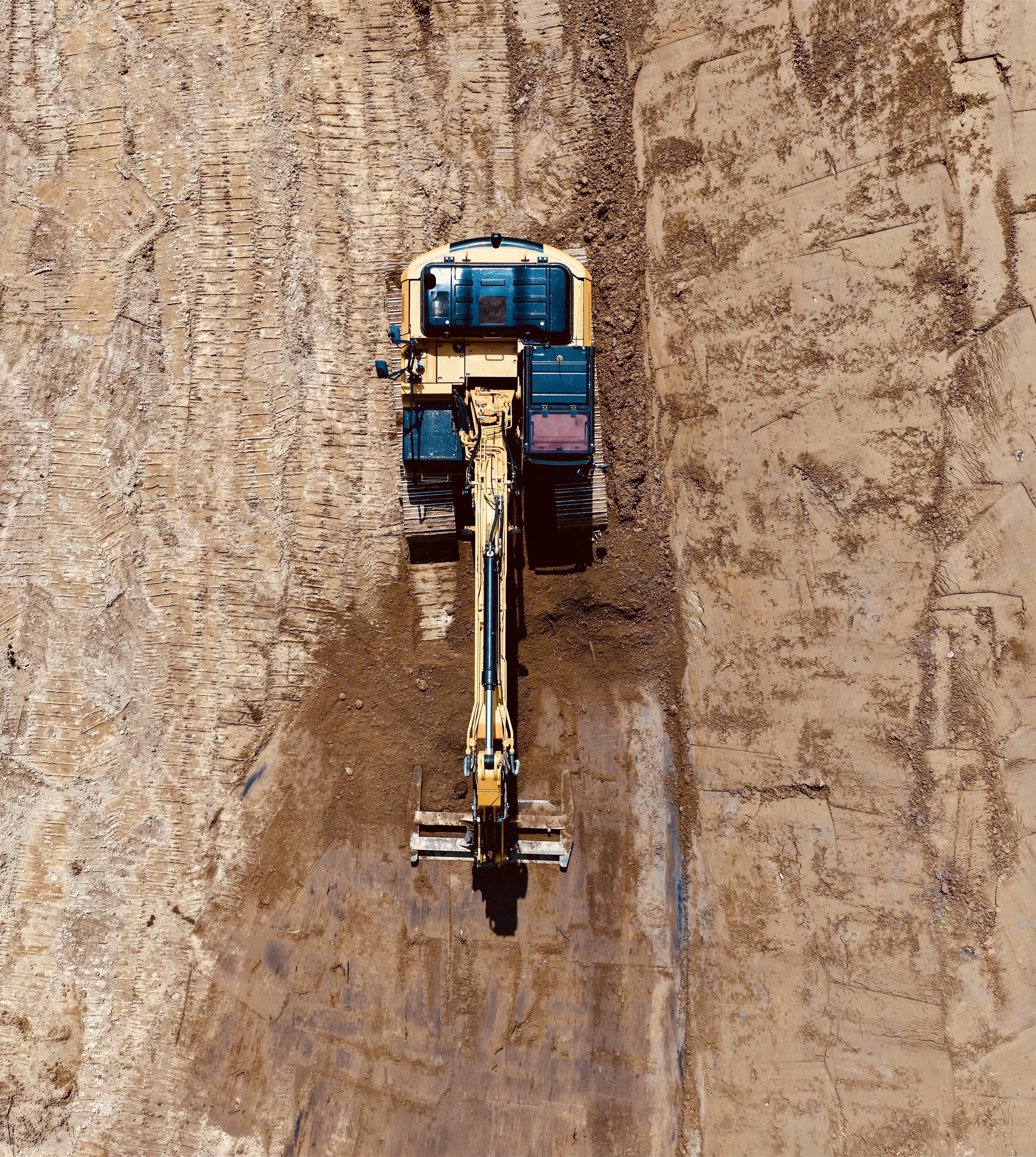 Aerial view of a yellow excavator working on a dirt construction site.