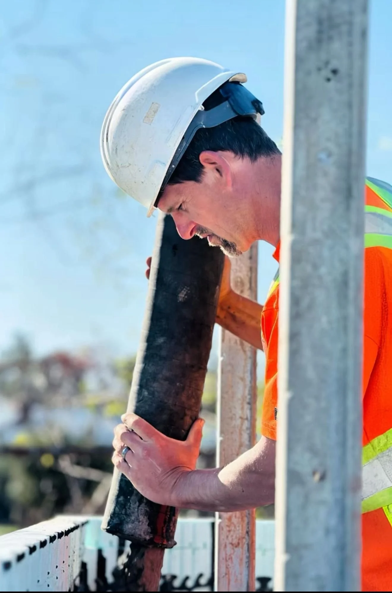 A construction worker wearing a white hard hat and orange safety vest is pouring concrete on an ICF wall structure.