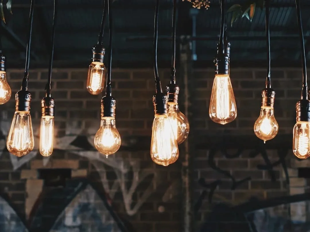 Hanging vintage Edison-style filament light bulbs in a dimly lit room with brick walls and graffiti.