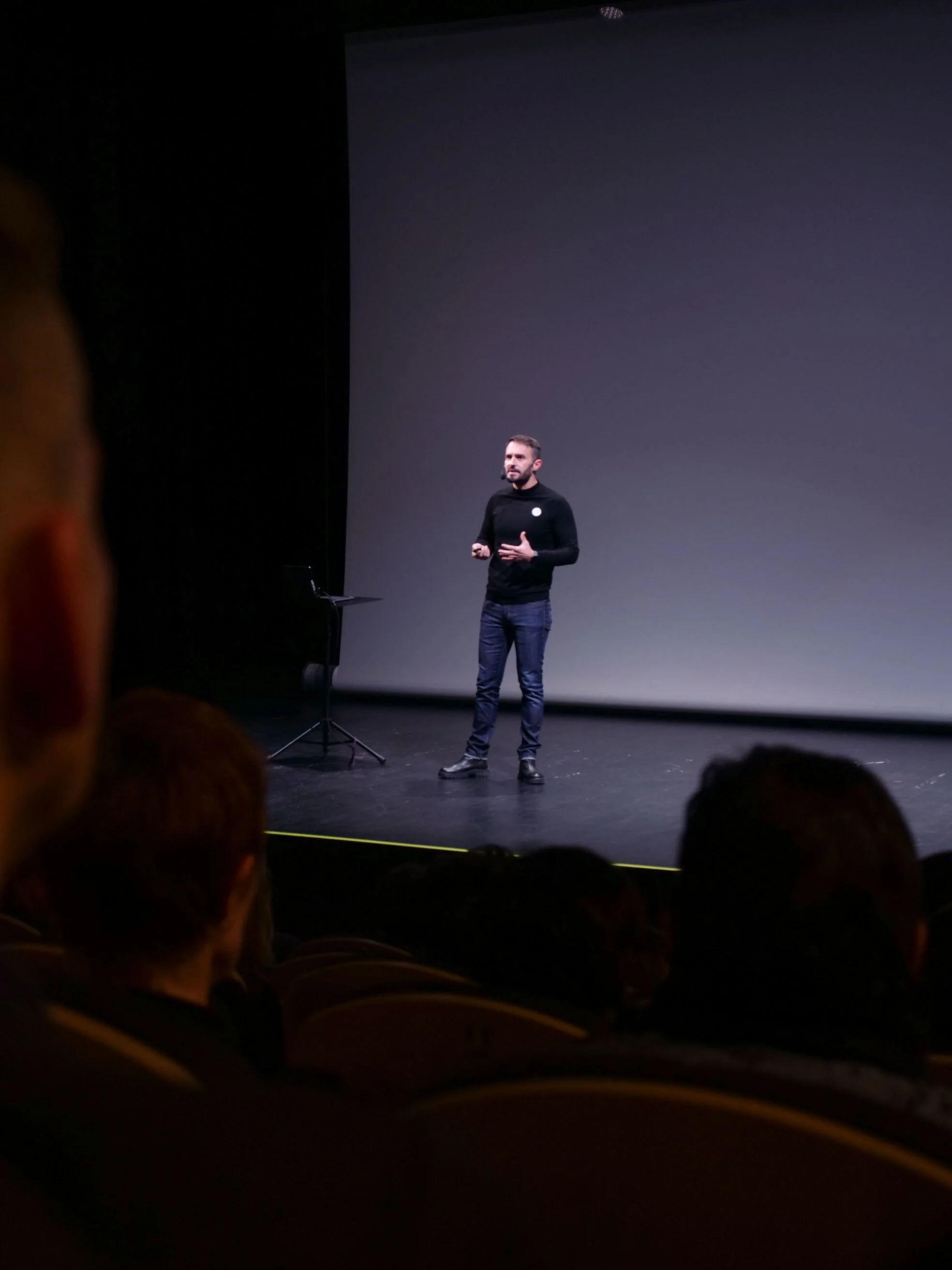 Hombre dando una presentación en un escenario oscuro frente a una audiencia.
