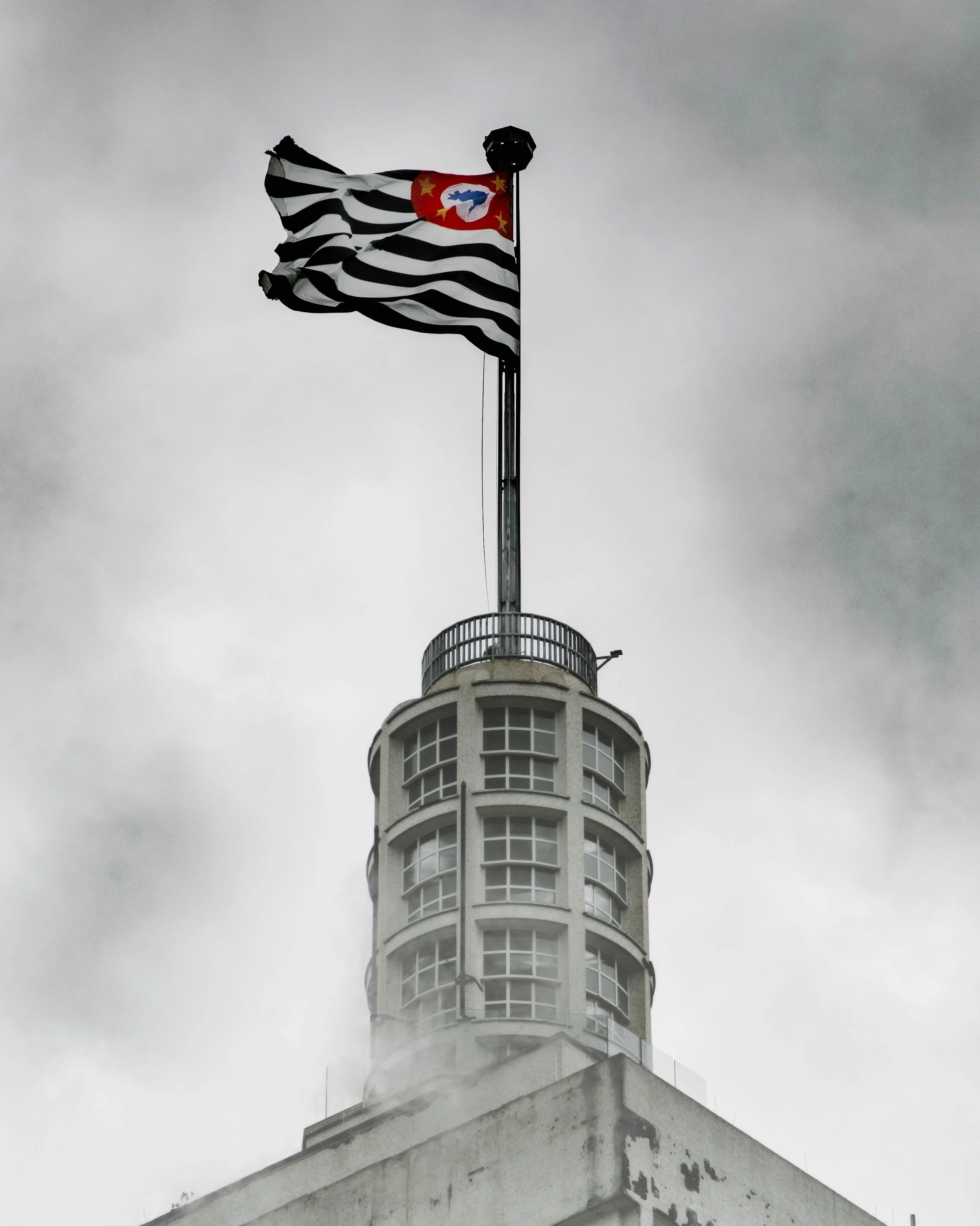 Bandeira do estado de São Paulo em um mastro no topo de um edifício em um dia nublado.