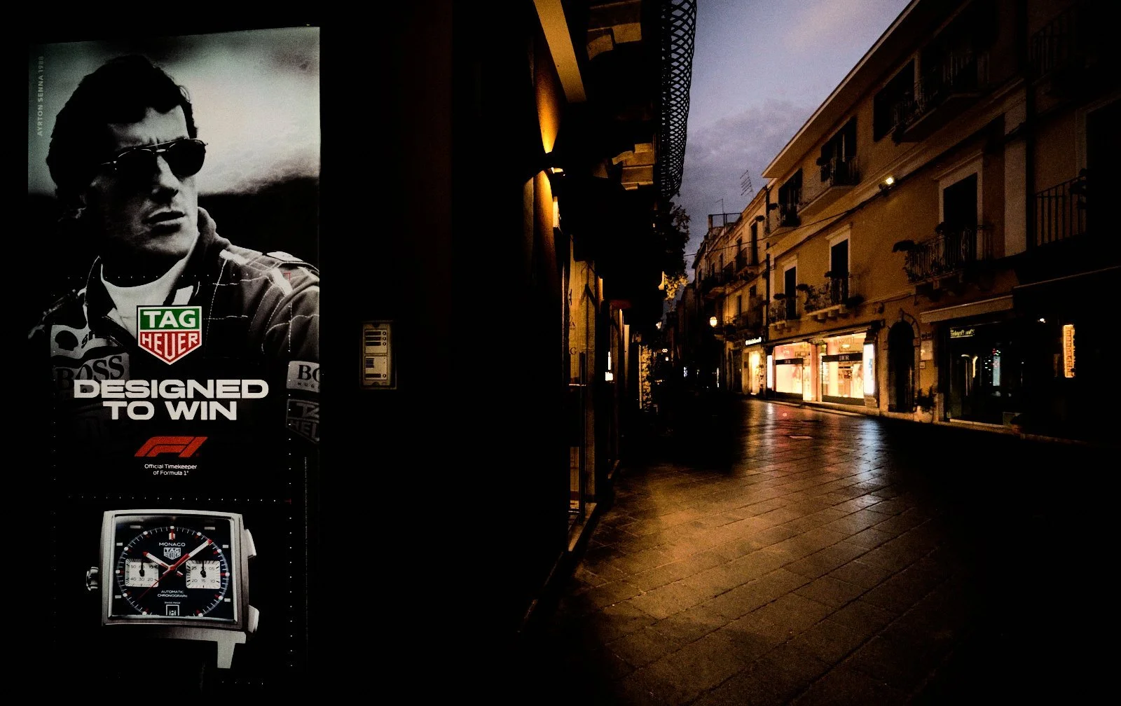 Black and white watch advertisement glowing beside an empty luxury shopping street at dawn in Taormina, Sicily — Provincia Malinconica by Tom Imio