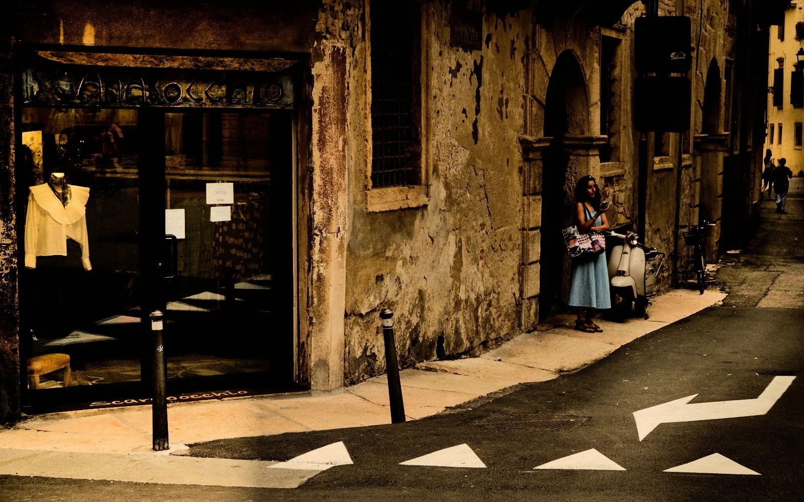 Woman waiting alone beside a scooter under a weathered archway in Verona, Italy — Provincia Malinconica by Tom Imio