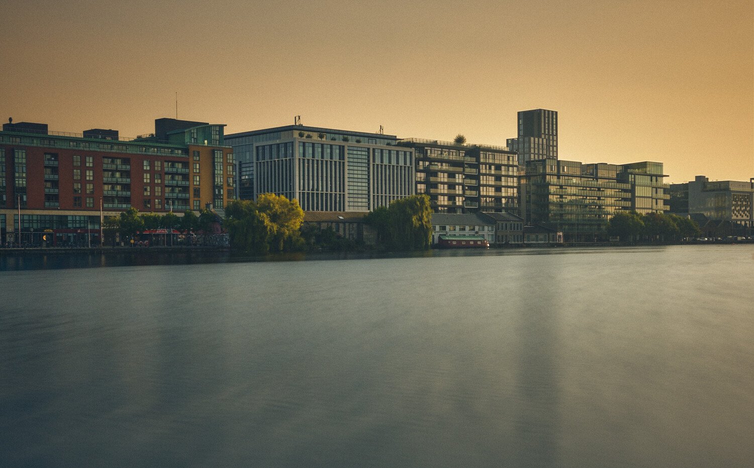 Cityscape of modern buildings along a waterfront at sunset.