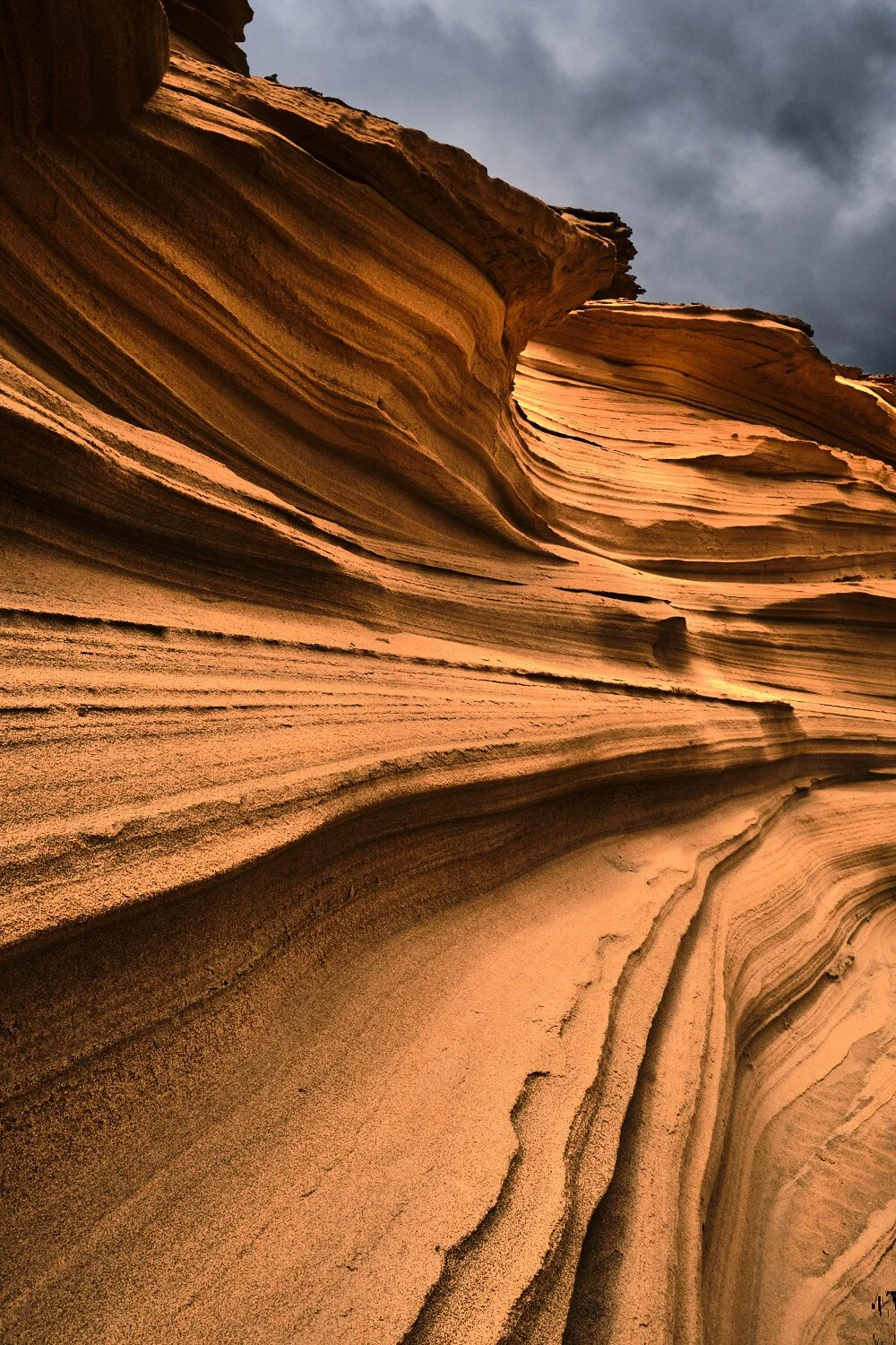 Layered sandstone formations in a canyon with a dark, cloudy sky above.
