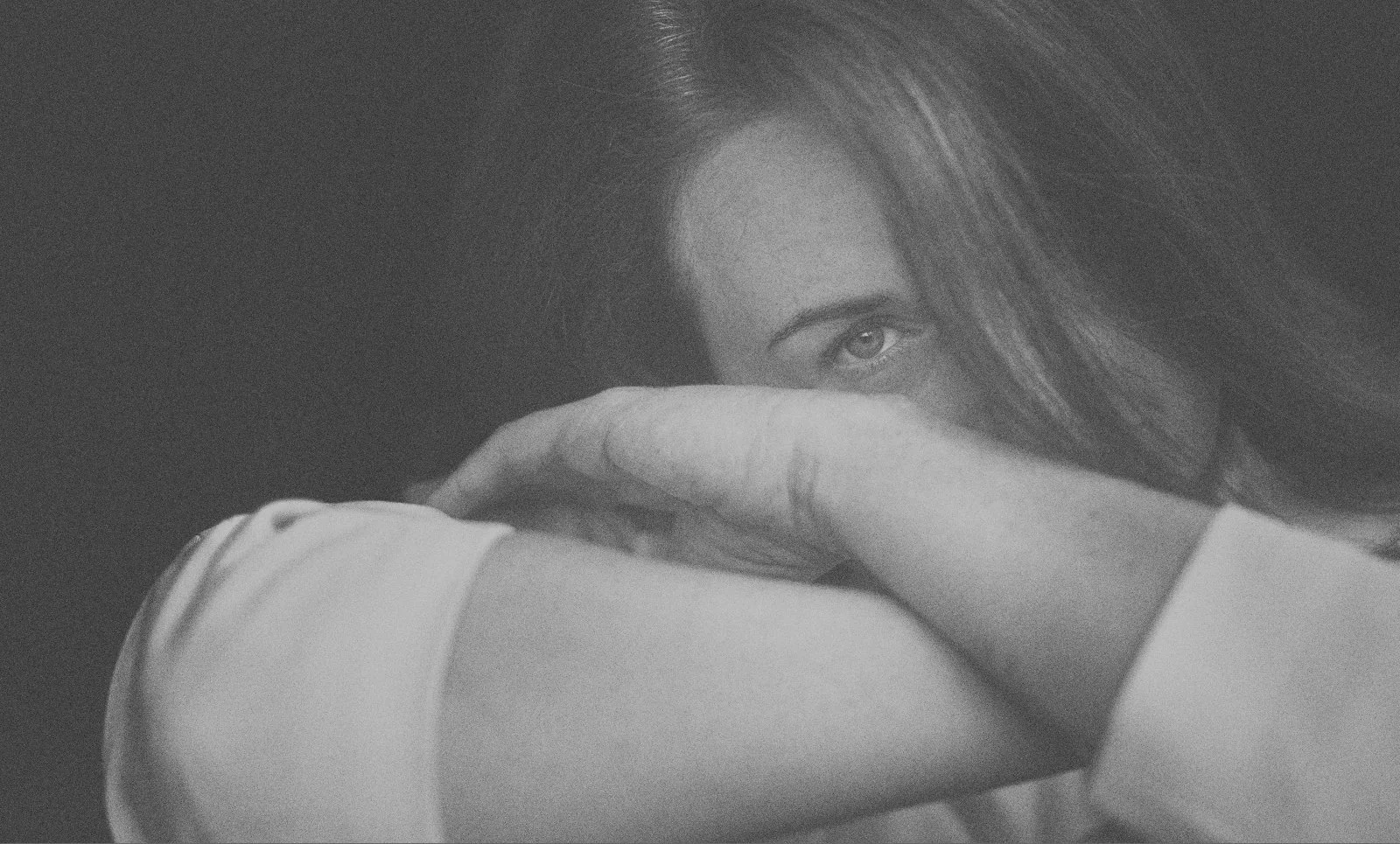 Black and white portrait of a woman shielding her face with her arm, one eye meeting the camera 