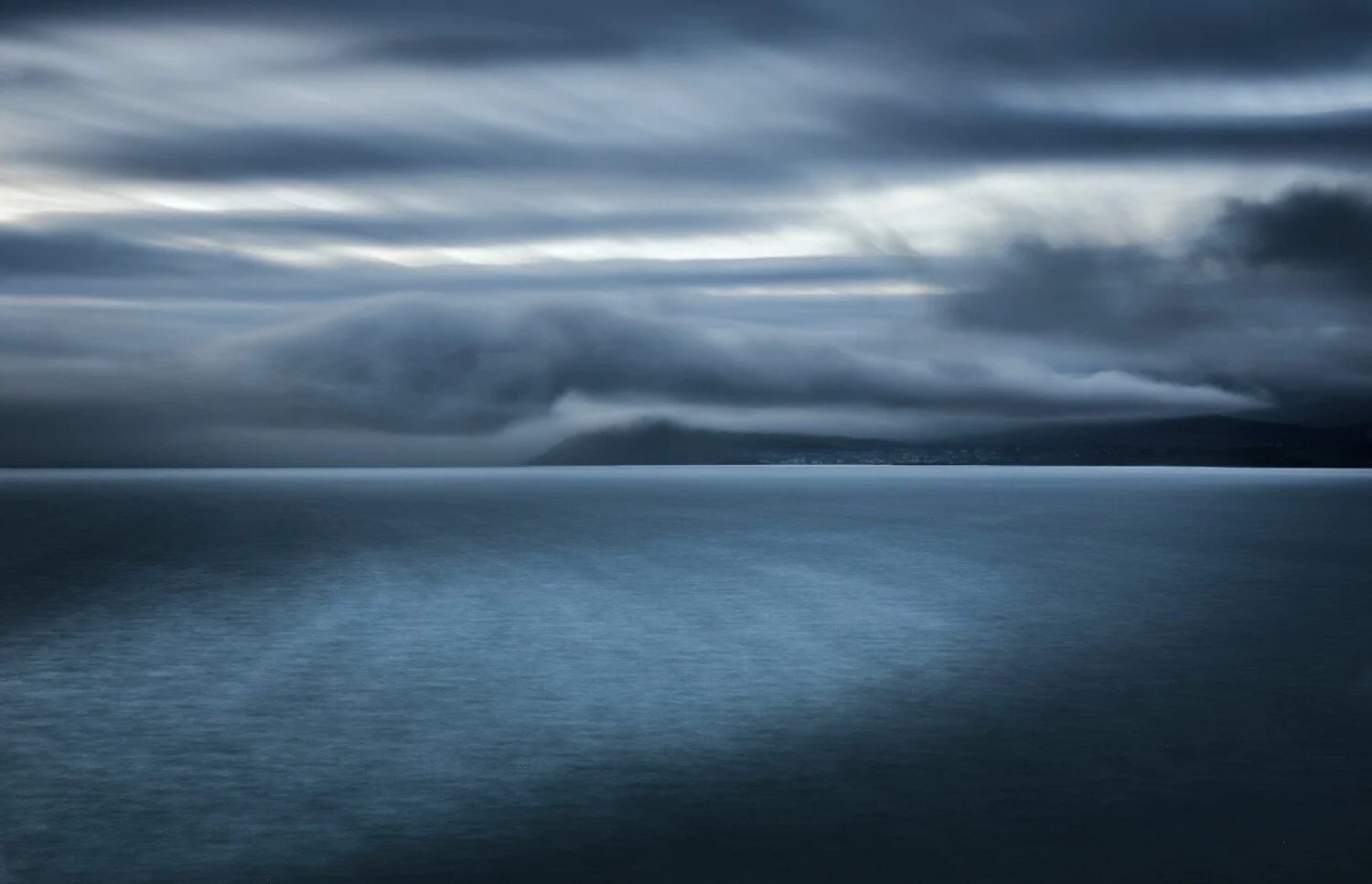 Dark, stormy sky with layered clouds over a calm ocean or lake under a moody atmosphere.
