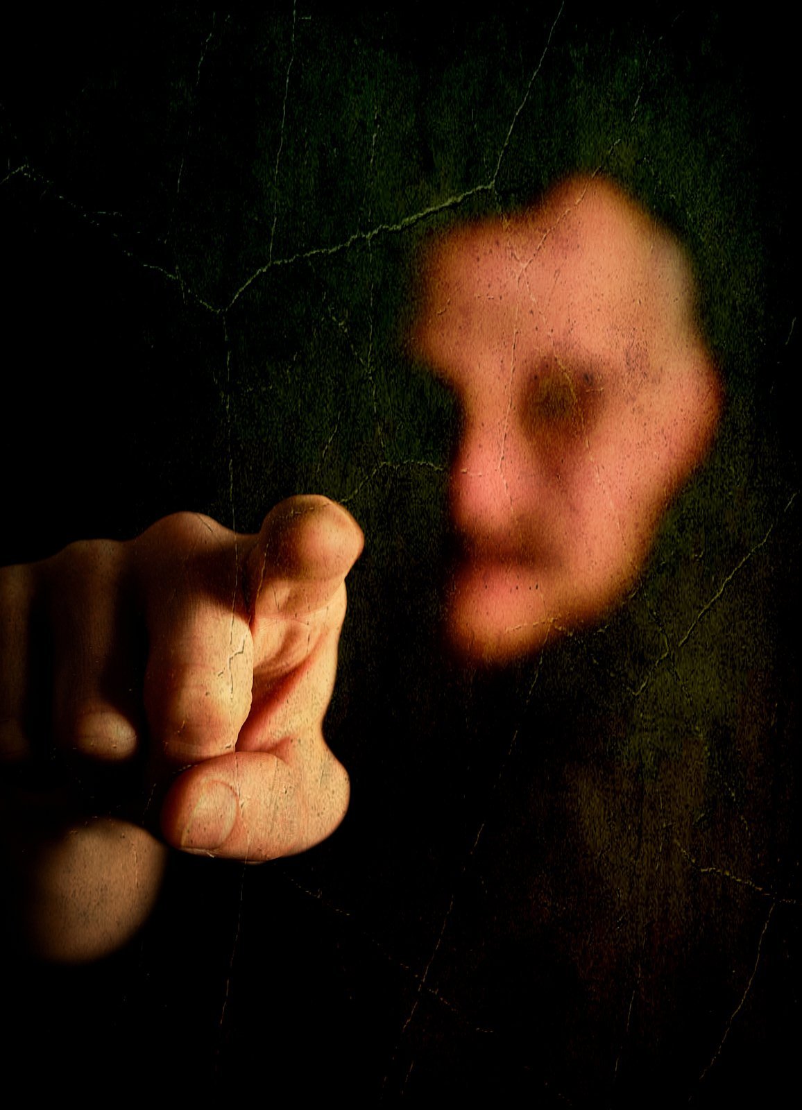 A close-up of a person's face behind a dark, cracked surface, with their hand pointing towards the camera.