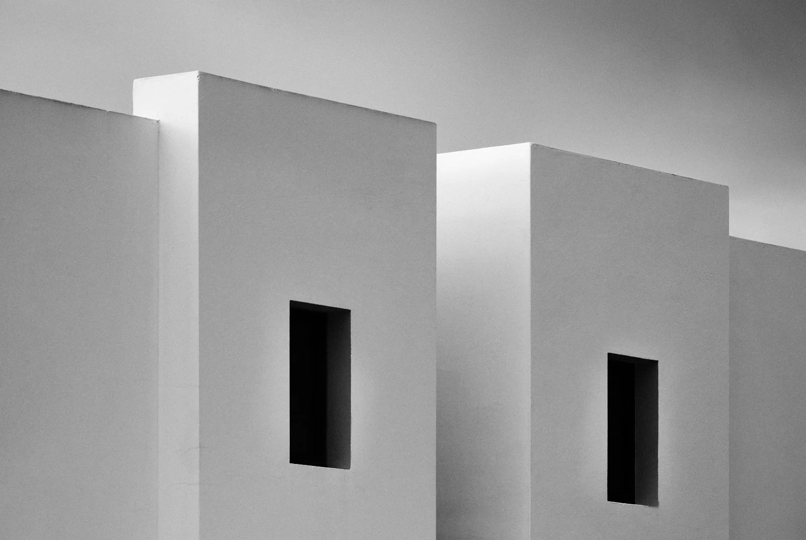 Minimalist white architectural buildings with rectangular windows, set against a gray sky.