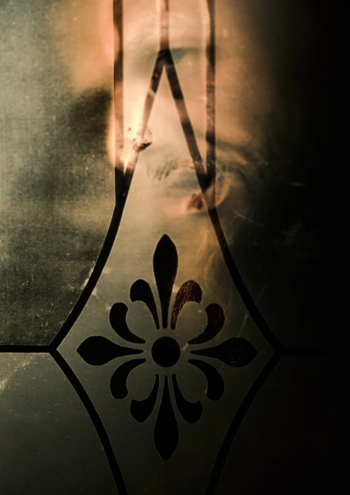 Close-up of a glass surface with a floral pattern and a human face reflection behind it.