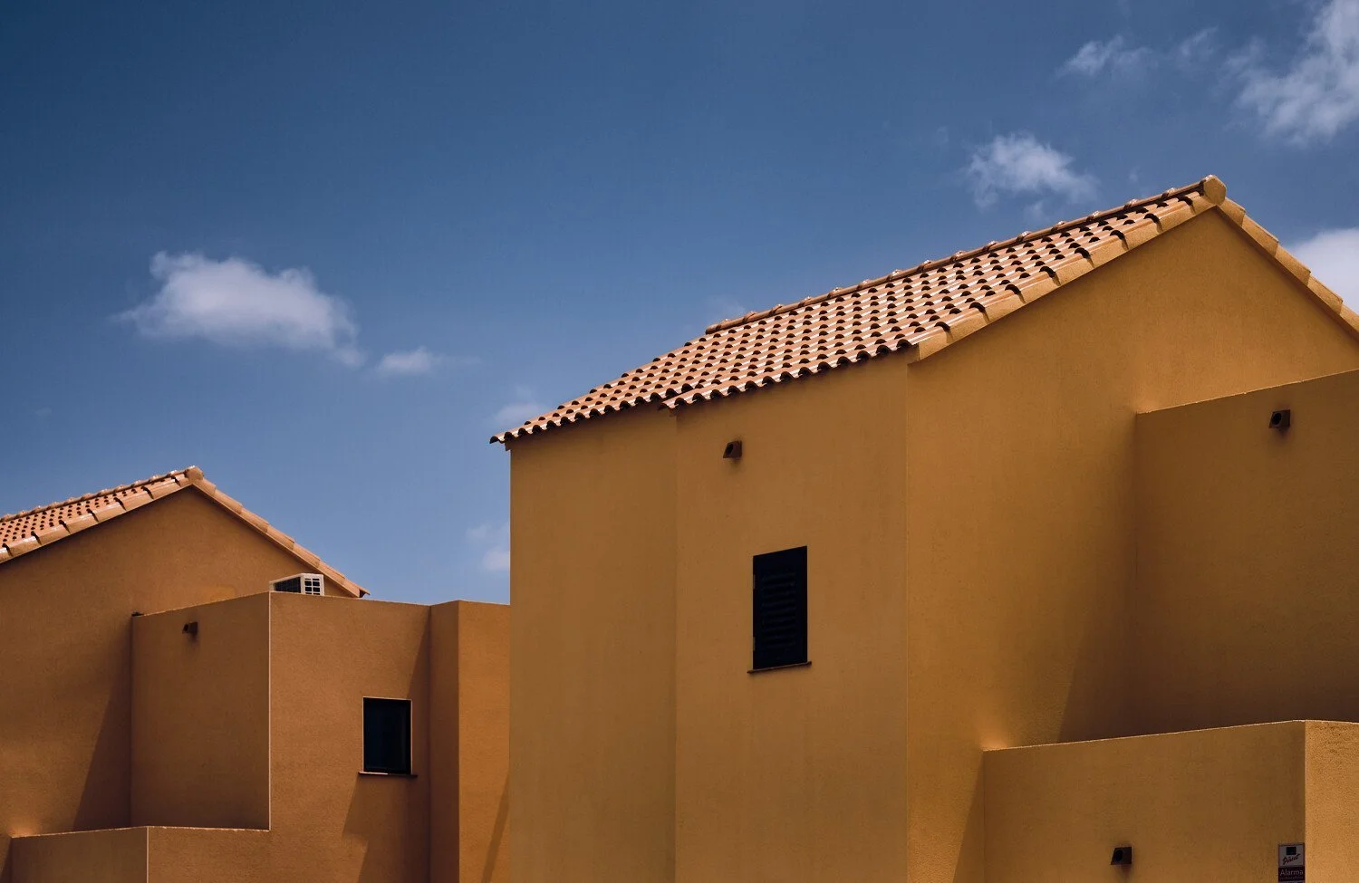Multiple yellow buildings with red-tiled roofs against a blue sky with a few clouds.